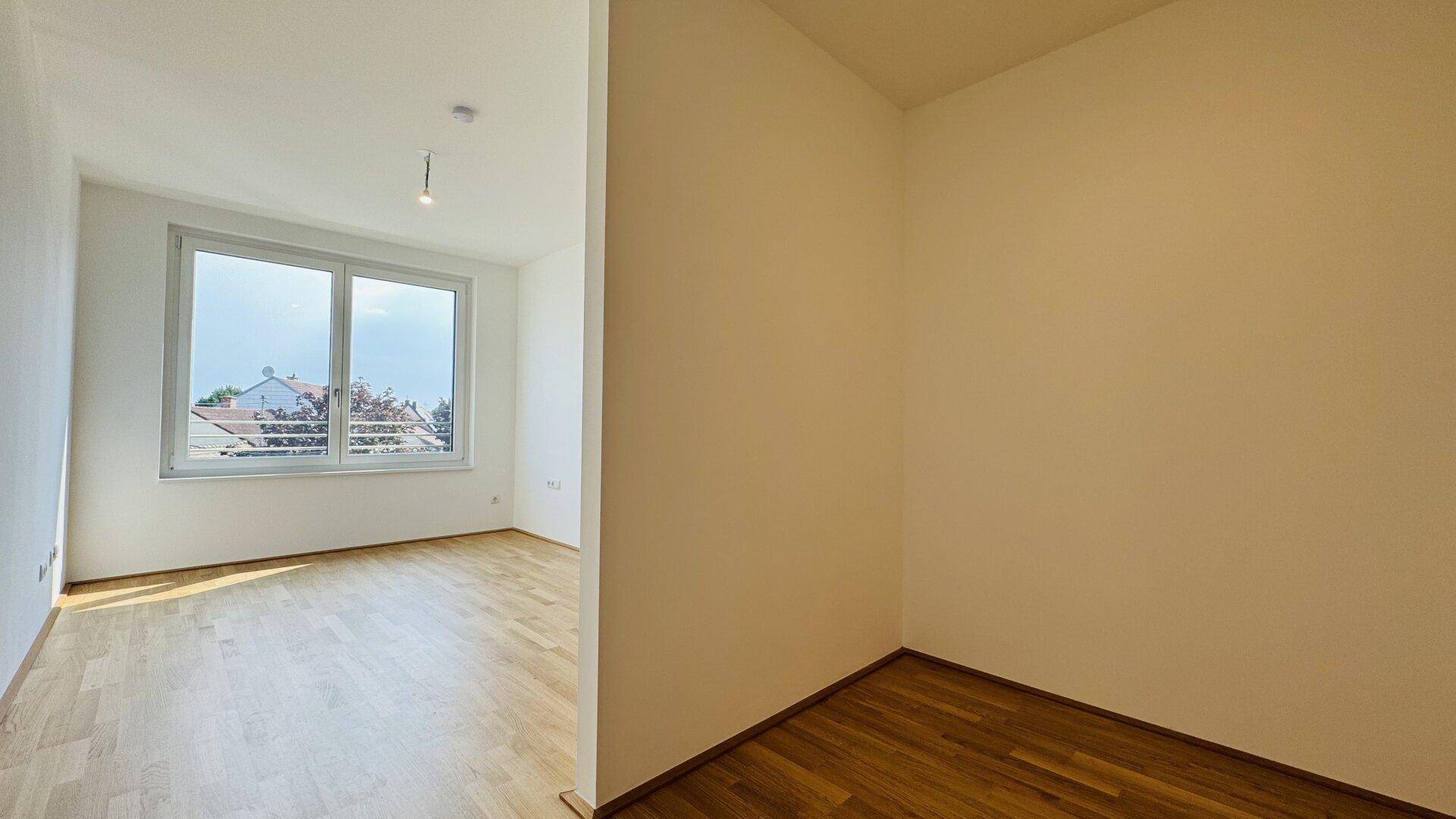 Helle, leere Räume mit Holzparkettboden und Fenstern, die Tageslicht hereinlassen.