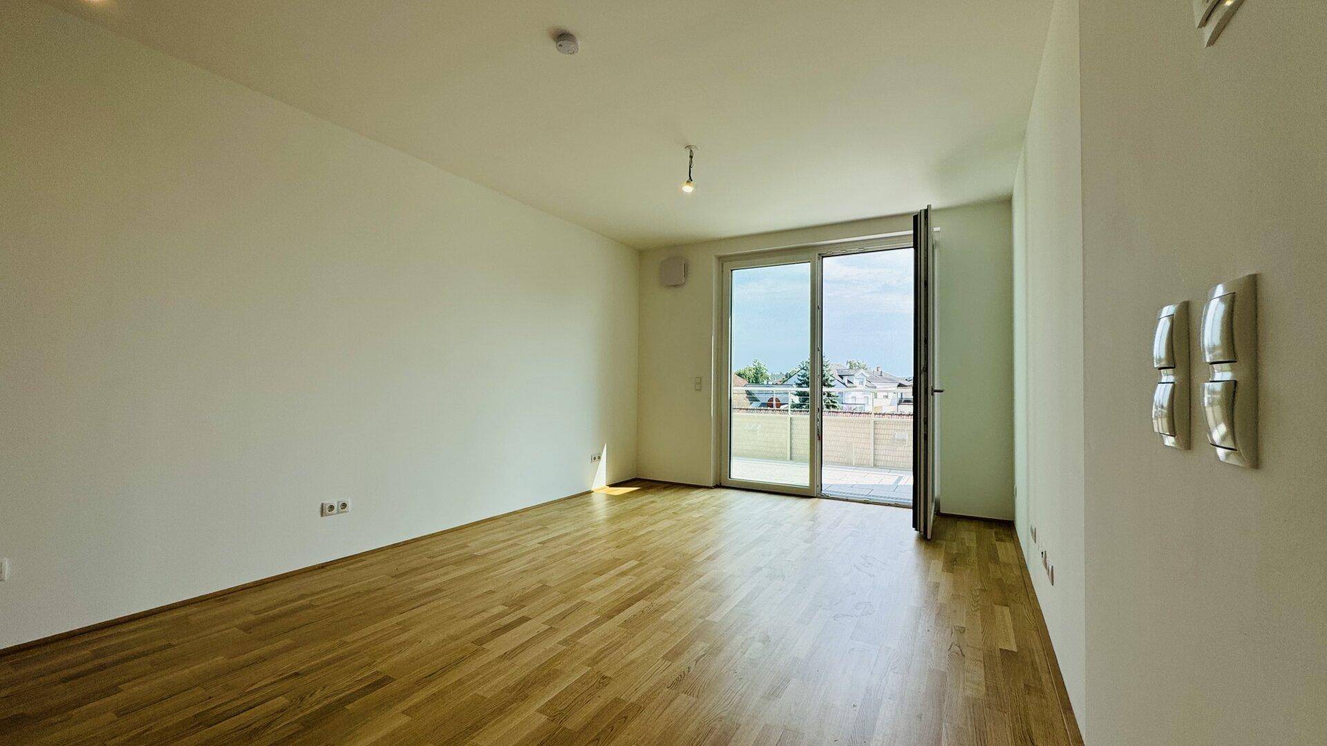 Heller Raum mit Holzparkettboden und Zugang zu einem Balkon oder einer Terrasse.