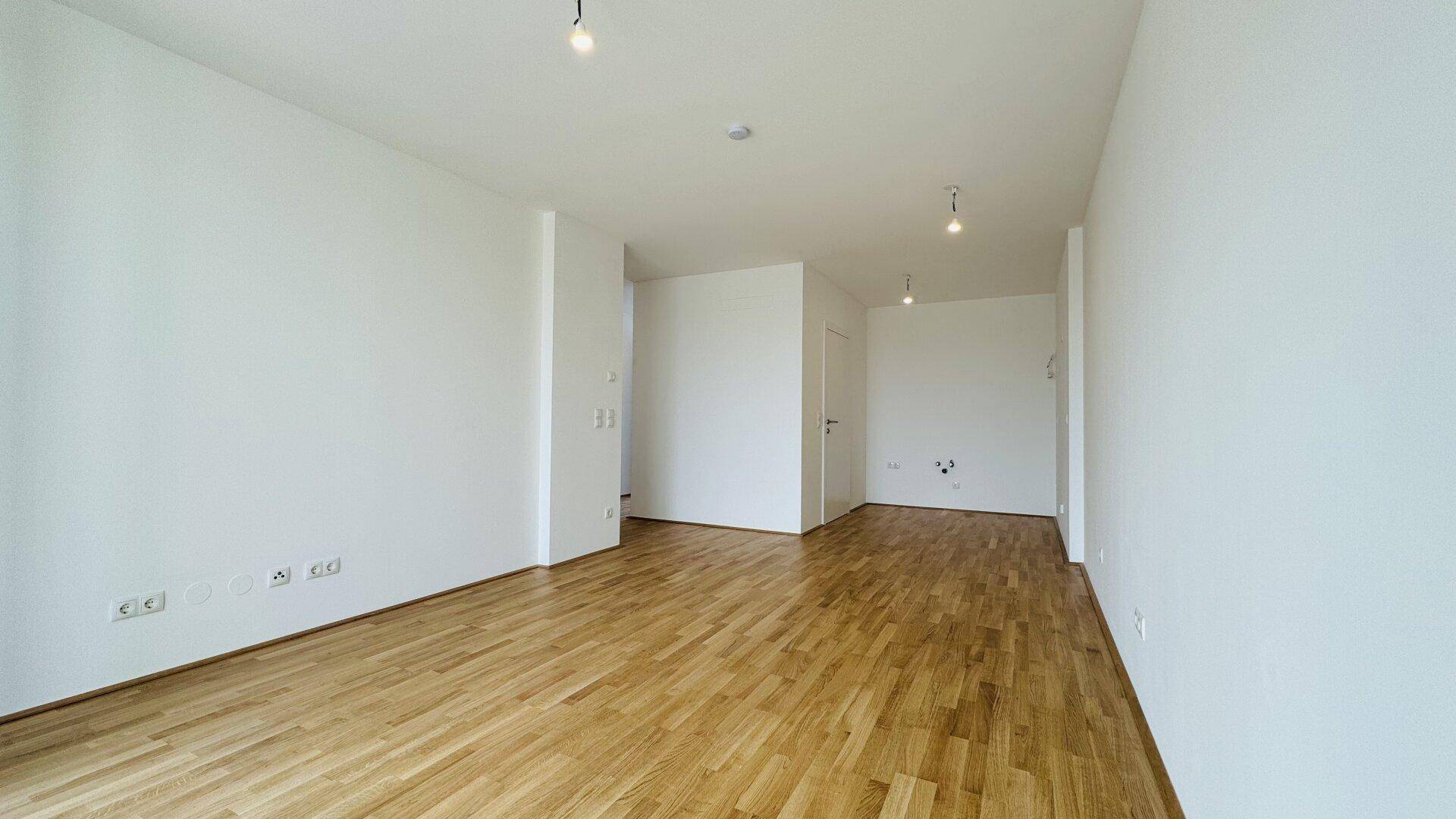 Geräumiger, heller Wohnbereich mit Holzparkettboden und mehreren Steckdosen.