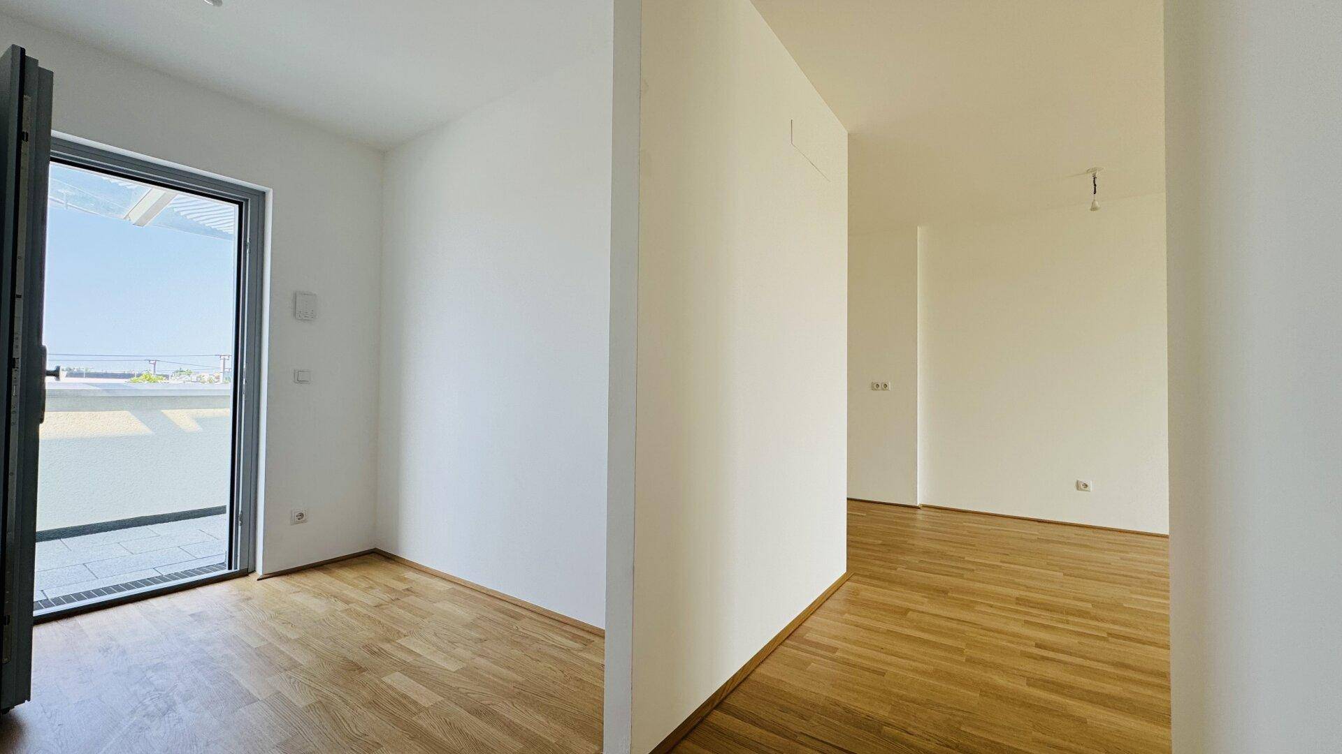 Heller Raum mit Holzparkettboden und großer Glastür, die auf einen Außenbereich führt.