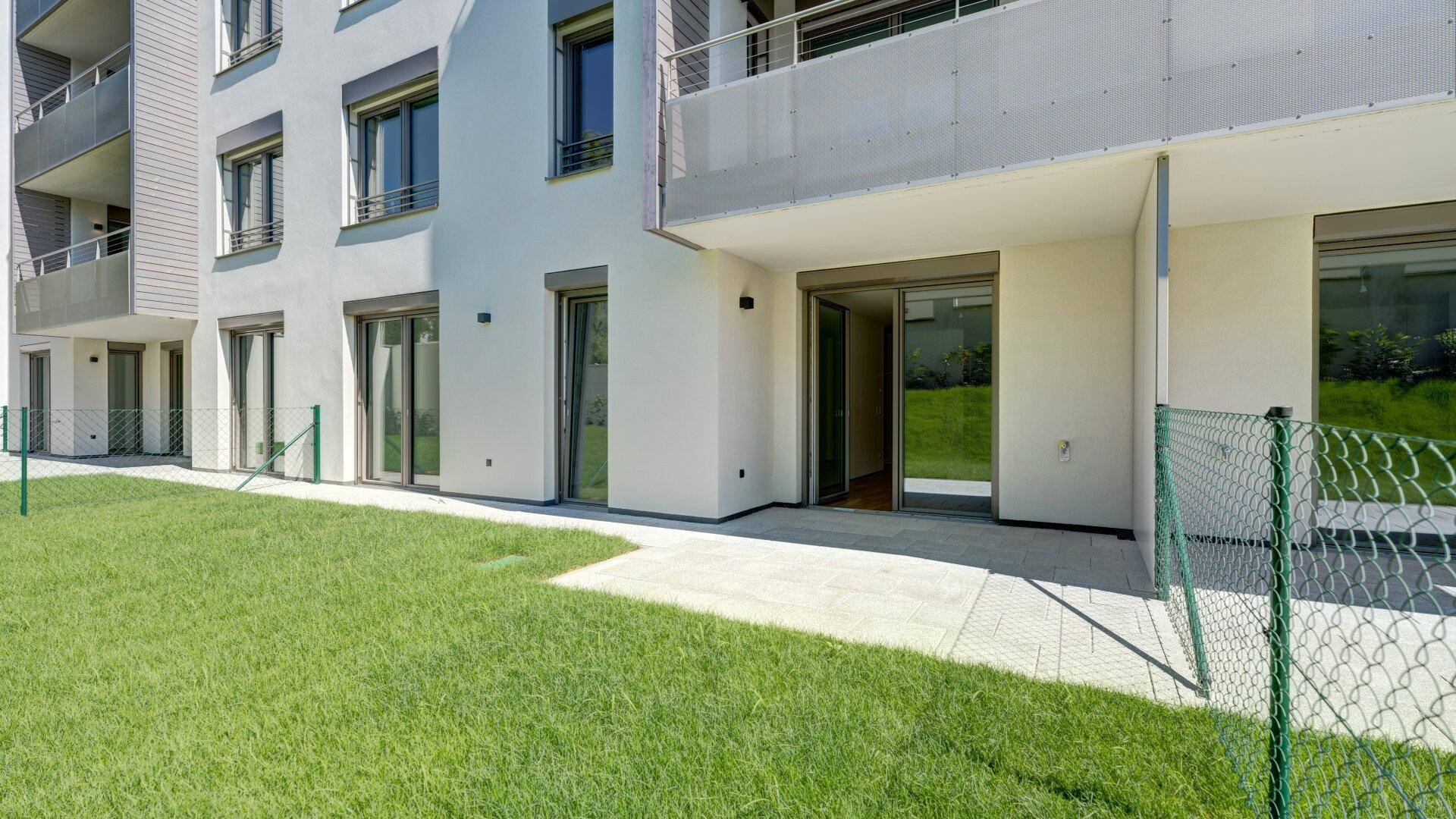 Erdgeschoss-Terrasse mit direktem Zugang zur Rasenfläche eines modernen Wohngebäudes.