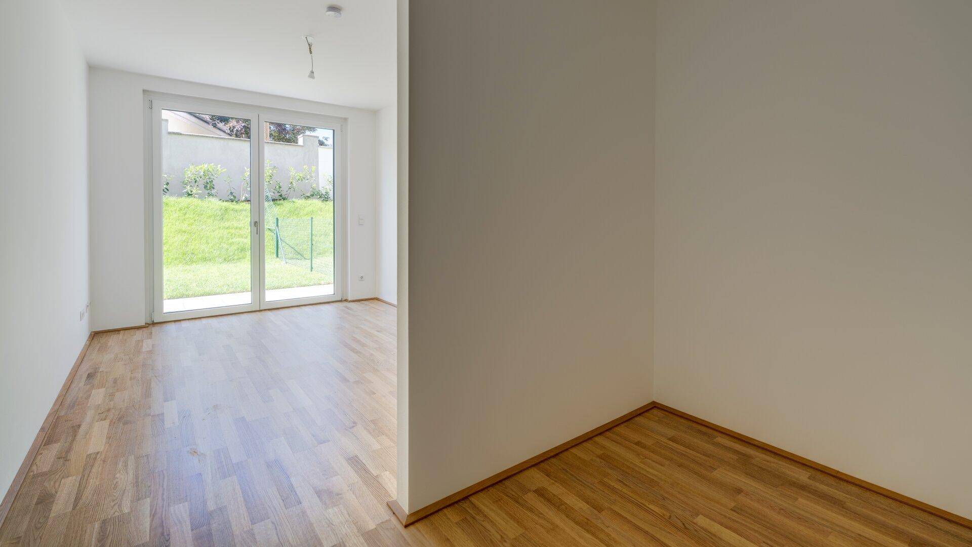 Offener Wohnbereich mit Holzboden und Blick durch die Terrassentür ins Grüne.