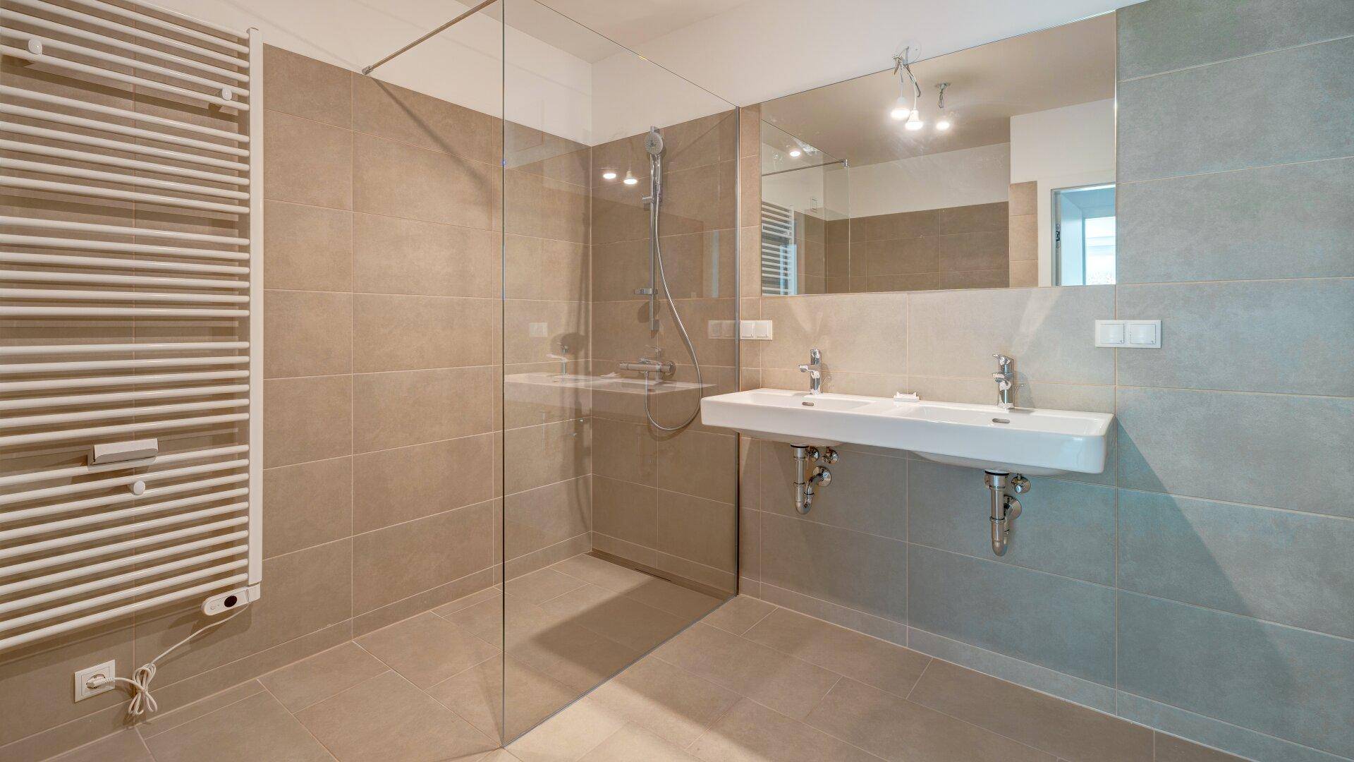 Modernes Badezimmer mit beigefarbenen Fliesen, großer Dusche und Doppelwaschbecken.