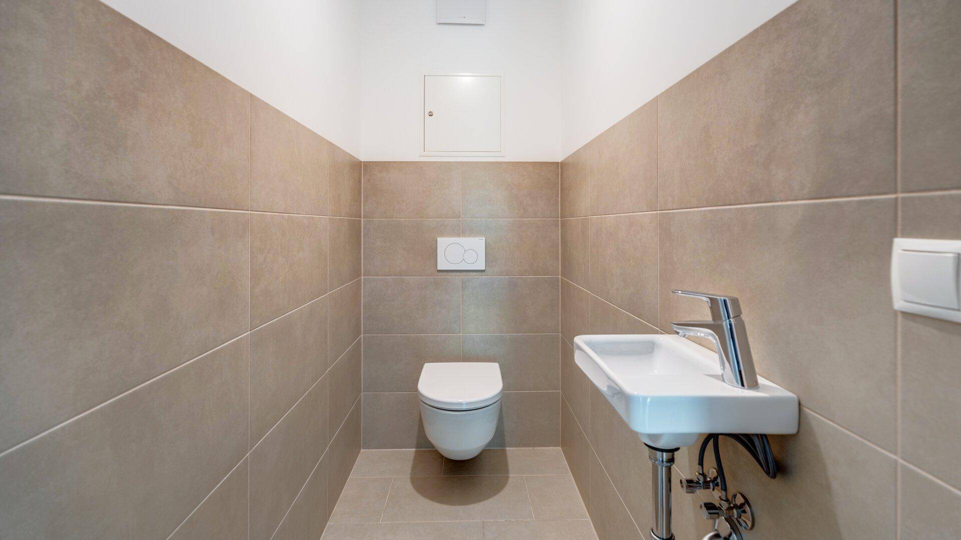 Modernes Gäste-WC mit Wand-WC, kleinem Waschbecken und beigefarbenen Wandfliesen.