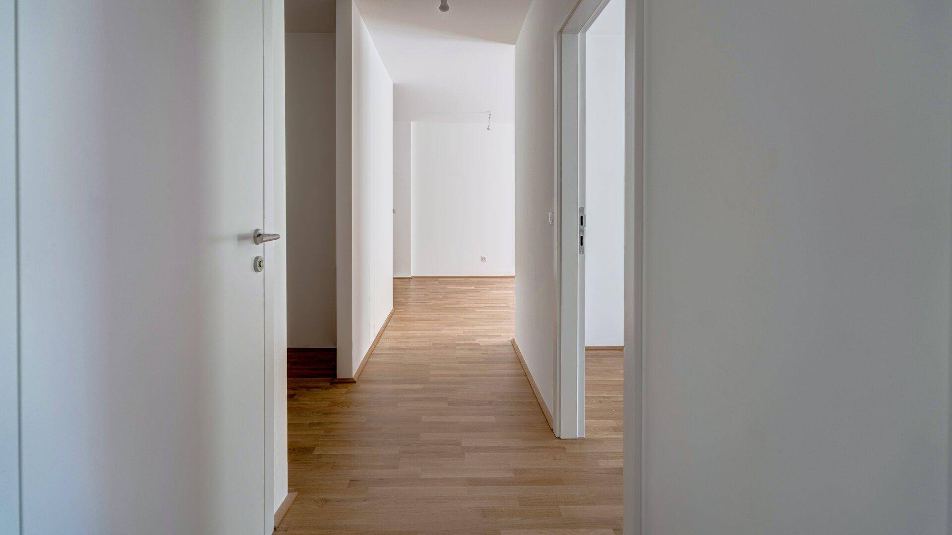 Heller Flur mit Holzboden und weißen Türen, der zu verschiedenen Räumen führt.