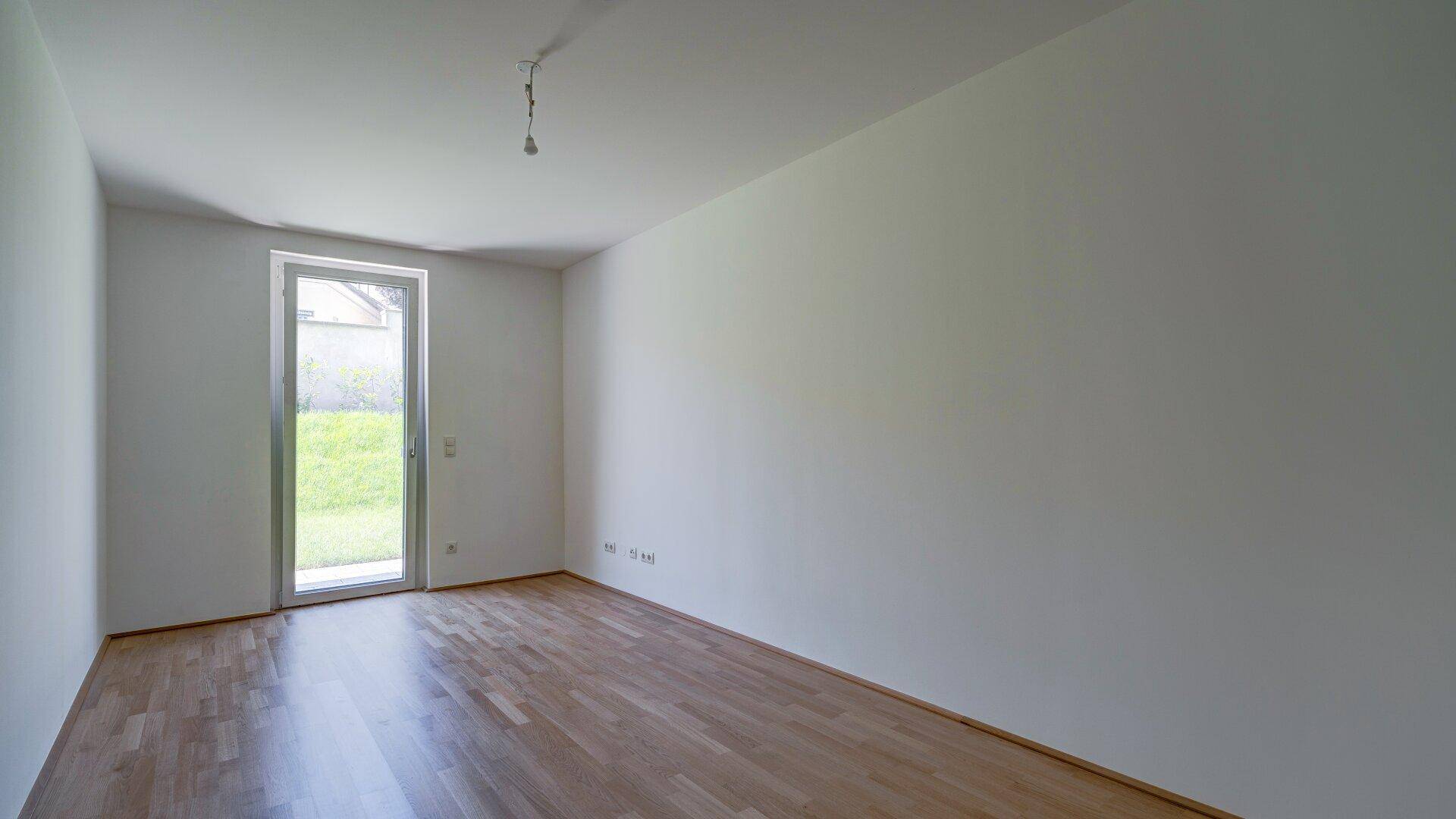 Helles Schlafzimmer mit Parkettboden und einer einzelnen Tür, die ins Freie führt.