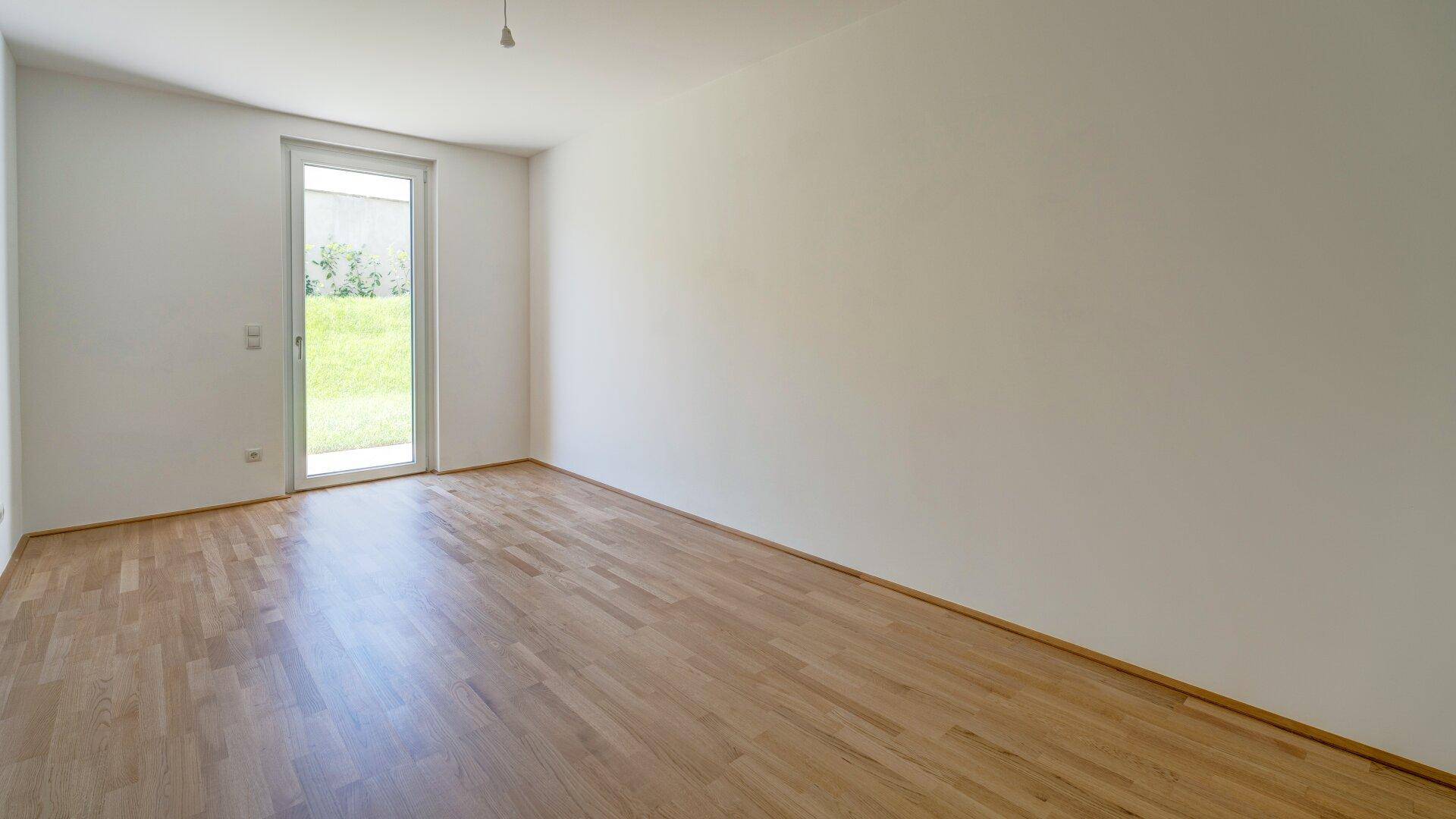 Helles Schlafzimmer mit Holzboden und Zugang zu einem kleinen Außenbereich.