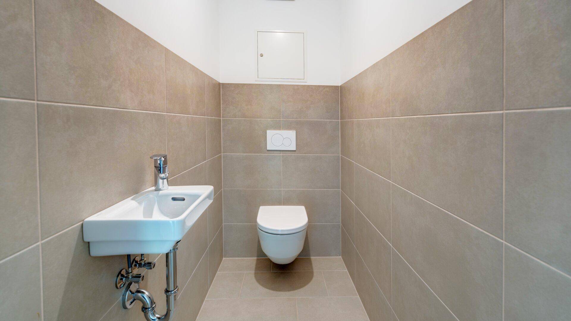 Modernes Gäste-WC mit Wand-WC und kleinem Waschbecken in neutralen Fliesen.