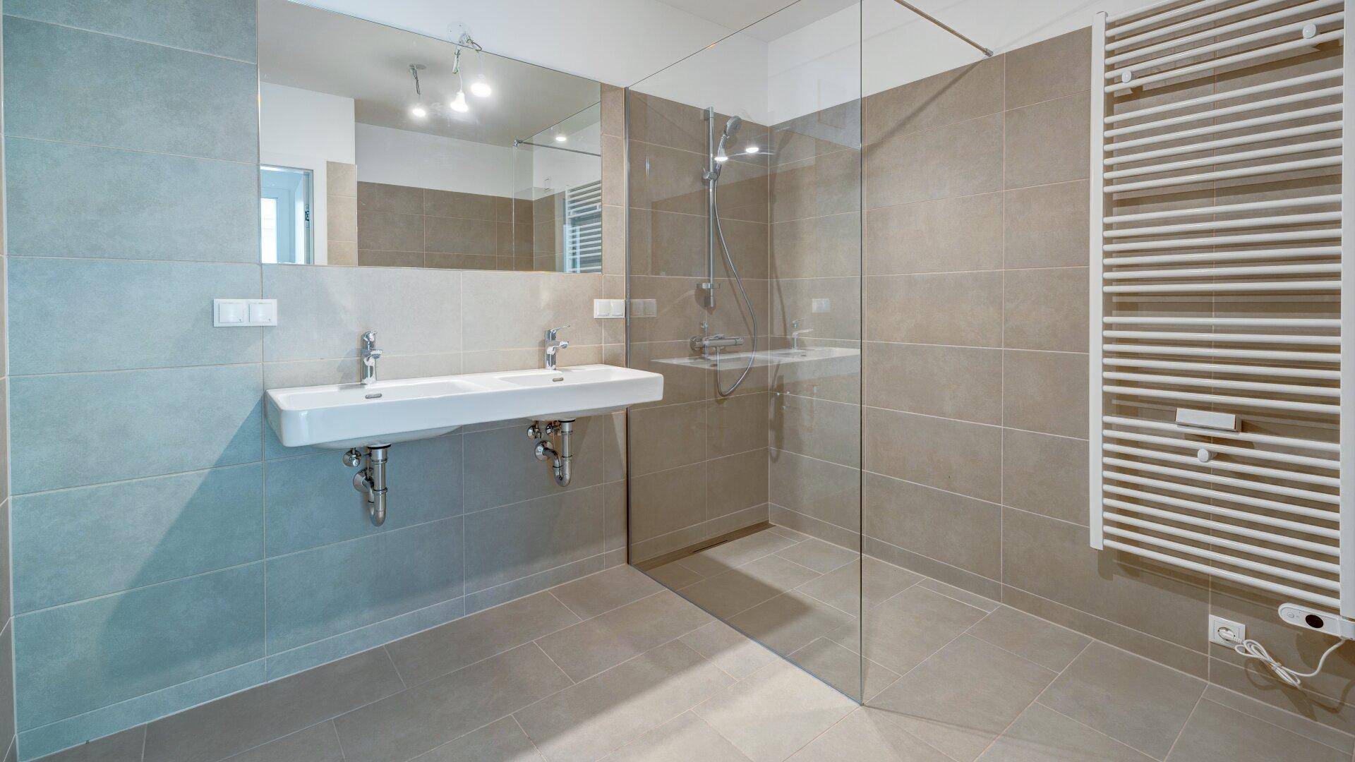 Modernes Badezimmer mit Doppelwaschbecken, großer Dusche und Handtuchheizkörper.