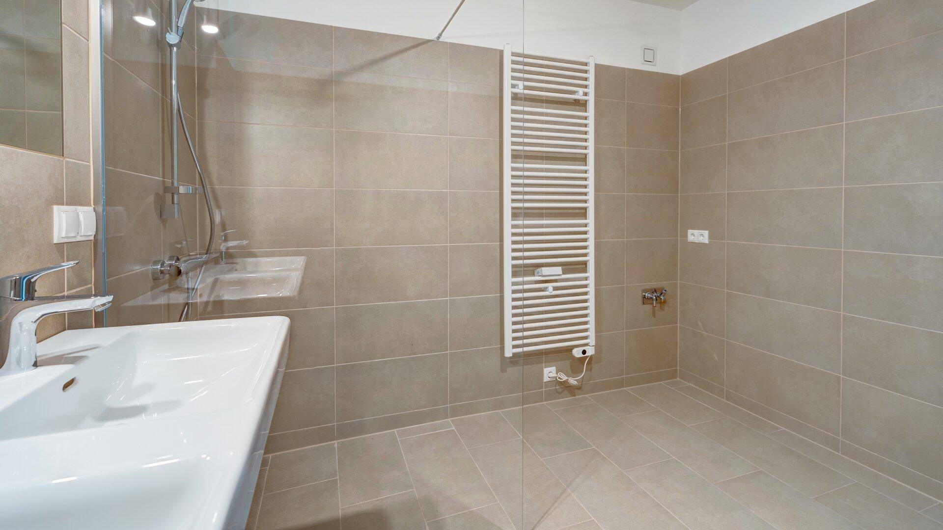 Helles Badezimmer mit großer Dusche, Handtuchheizkörper und modernen Fliesen.