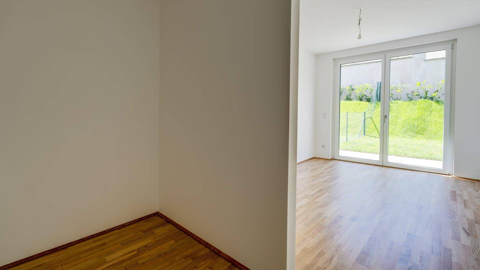 Teilansicht eines hellen Raumes mit Holzboden und Blick auf den Garten.