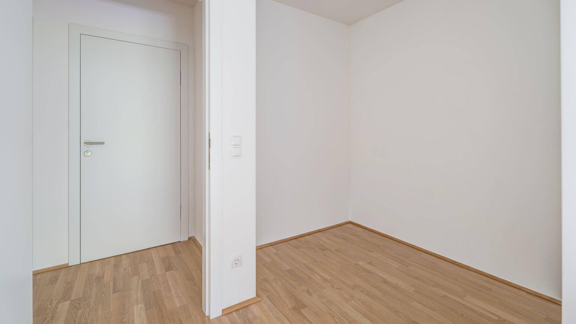 Kleiner, heller Raum mit Holzboden und einer weißen Tür.