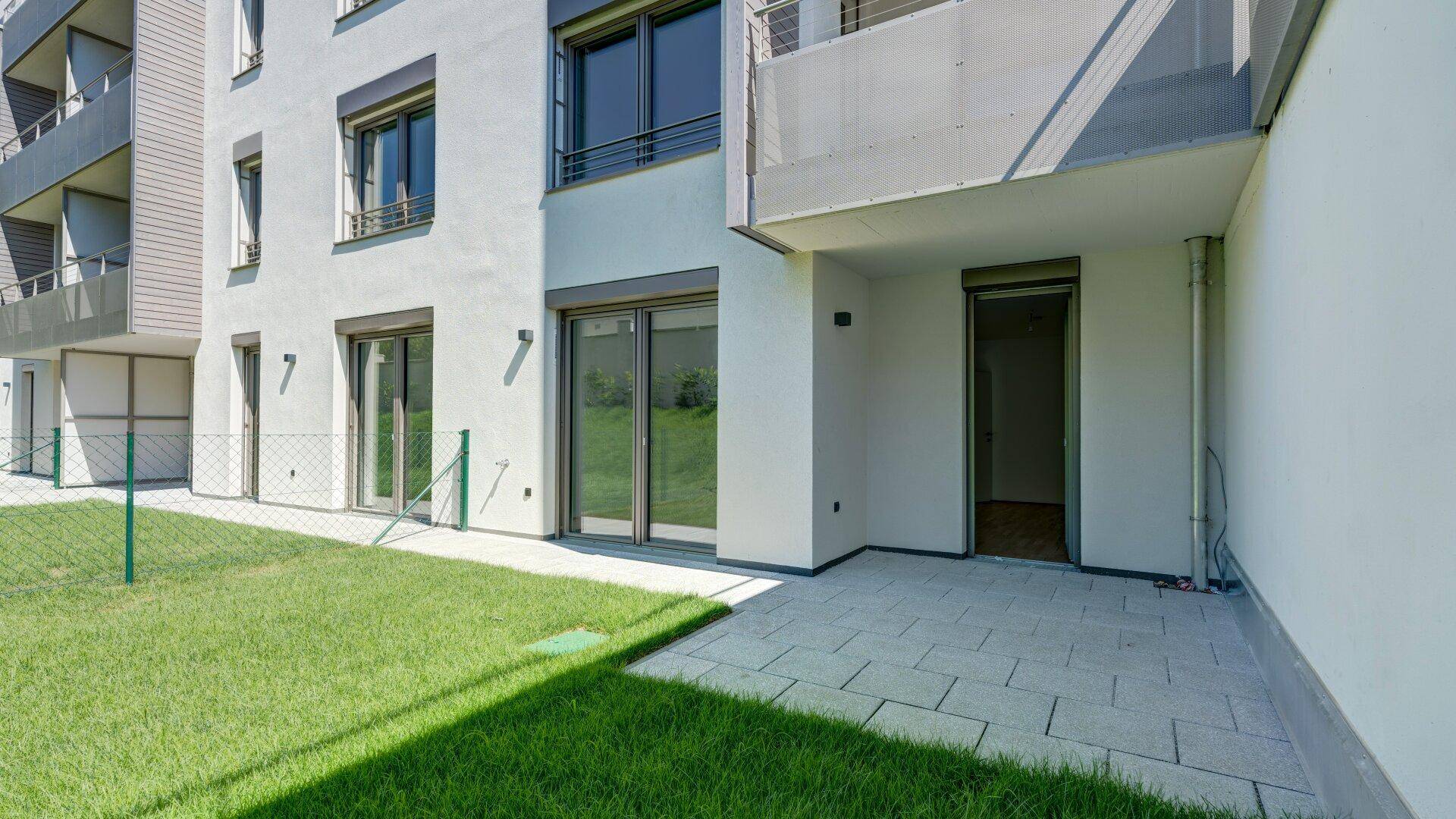 Außenansicht eines modernen Gebäudes mit Zugang zu einer kleinen privaten Rasenfläche und Terrasse.