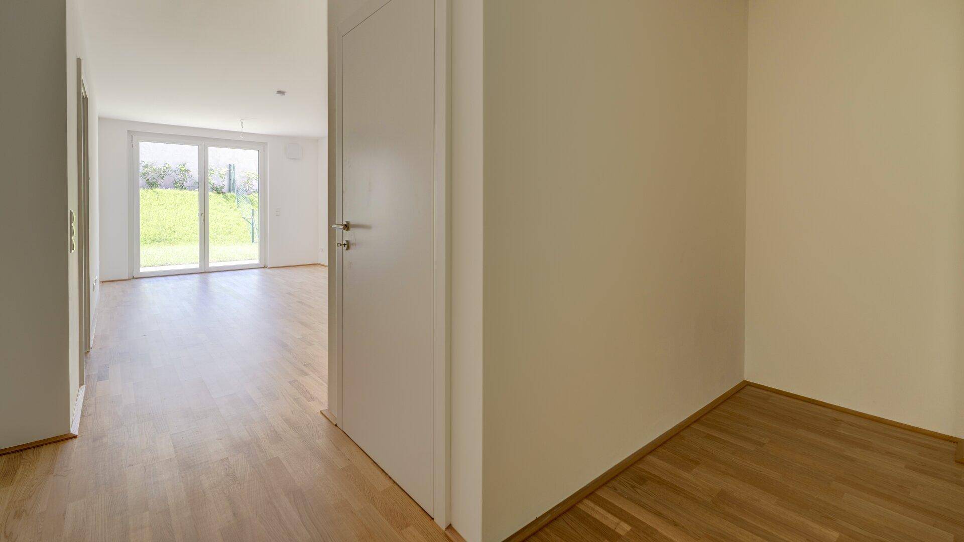 Heller Flur mit Holzboden, weißen Wänden und Blick in einen angrenzenden Wohnbereich.