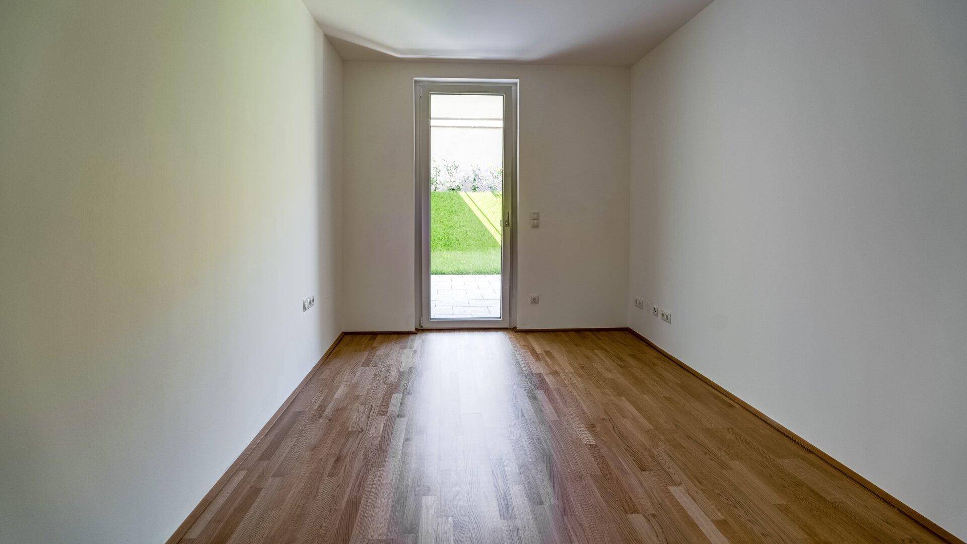 Helles Zimmer mit Holzboden und Zugang zu einem kleinen Außenbereich, ideal als Schlafzimmer.