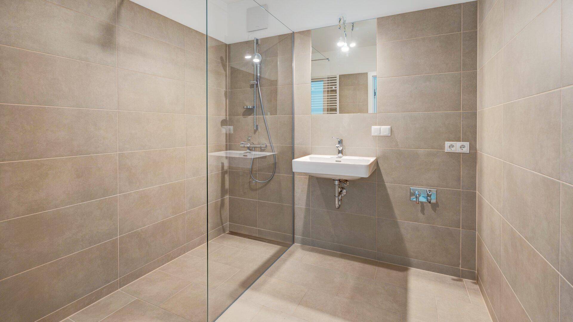 Modernes Badezimmer mit beigefarbenen Fliesen, ebenerdiger Dusche und elegantem Waschbecken.