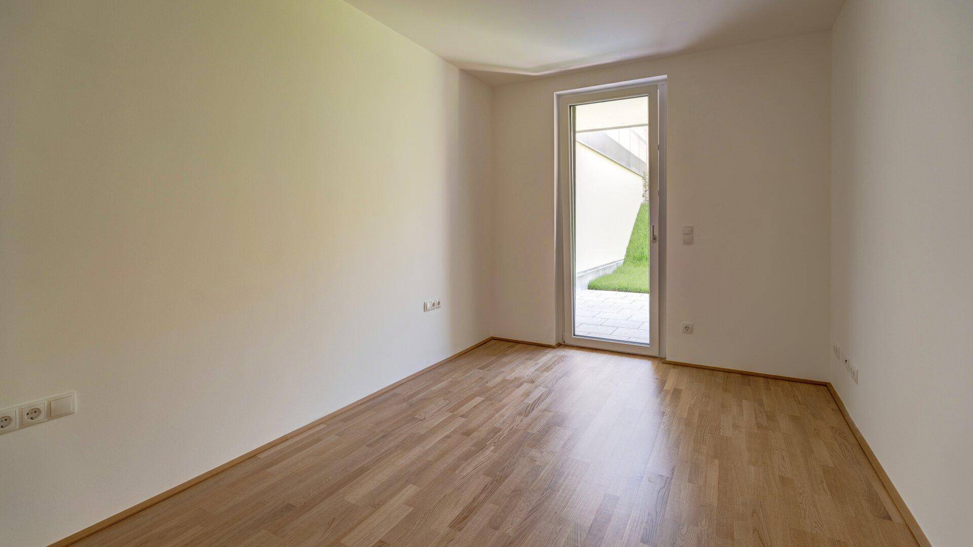 Leeres Zimmer mit Holzboden, weißen Wänden und Blick ins Grüne, vielseitig nutzbar.