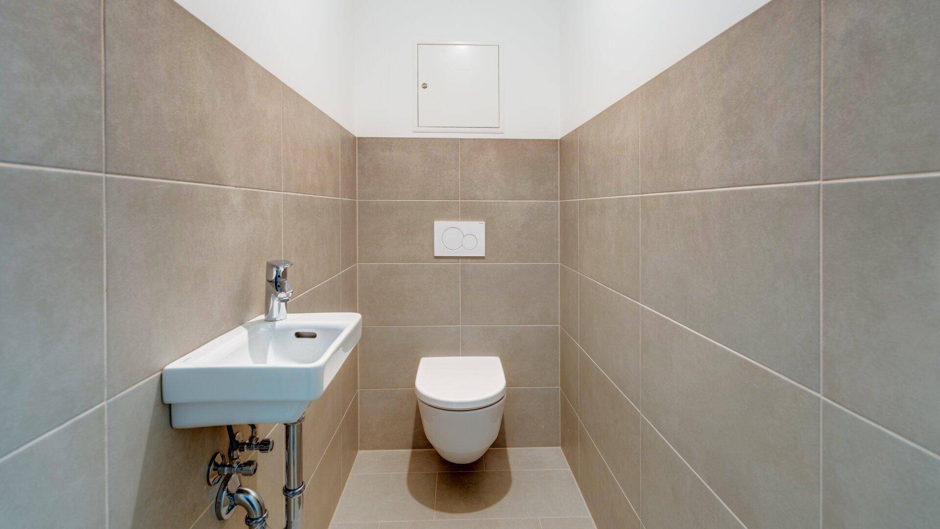 Modernes Gäste-WC mit Wand-WC, kleinem Waschbecken und beigefarbenen Wandfliesen.