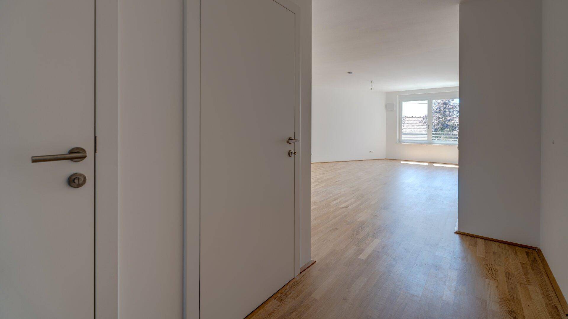 Heller Flur mit Holzparkettboden, der in einen geräumigen Wohnbereich mit viel Tageslicht führt.
