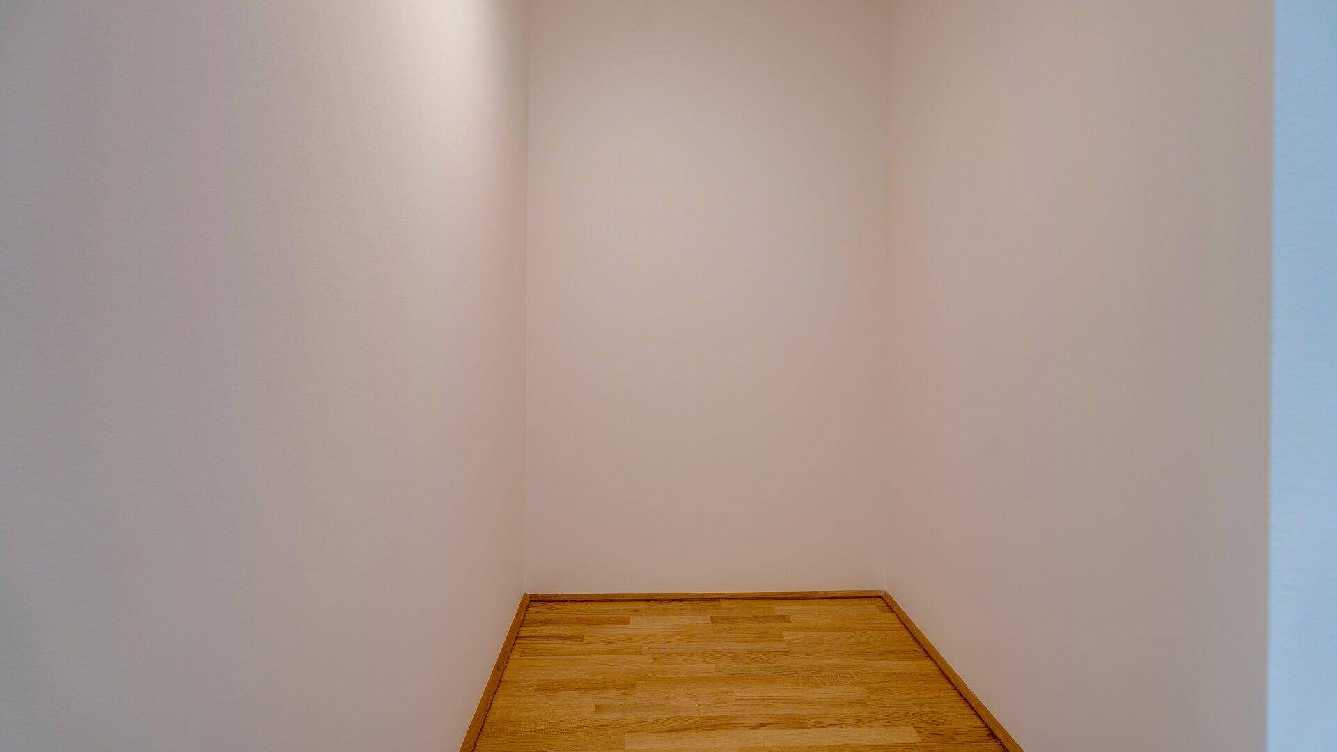 Kleiner, leerer Raum mit Holzparkettboden und weißen Wänden, ideal als Abstellraum oder begehbarer Kleiderschrank.