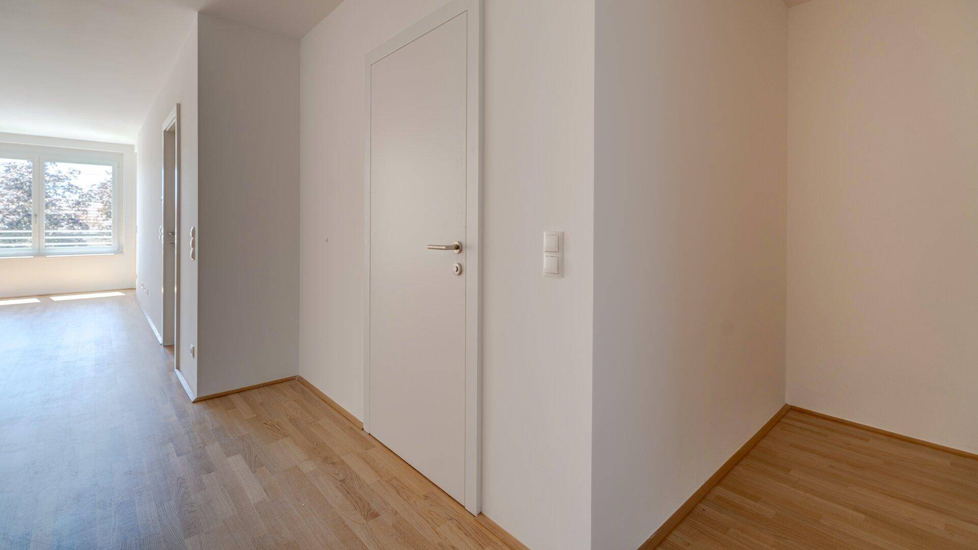 Geräumiger Flur mit hellem Holzparkettboden und weißen Wänden, der zu weiteren Zimmern führt.