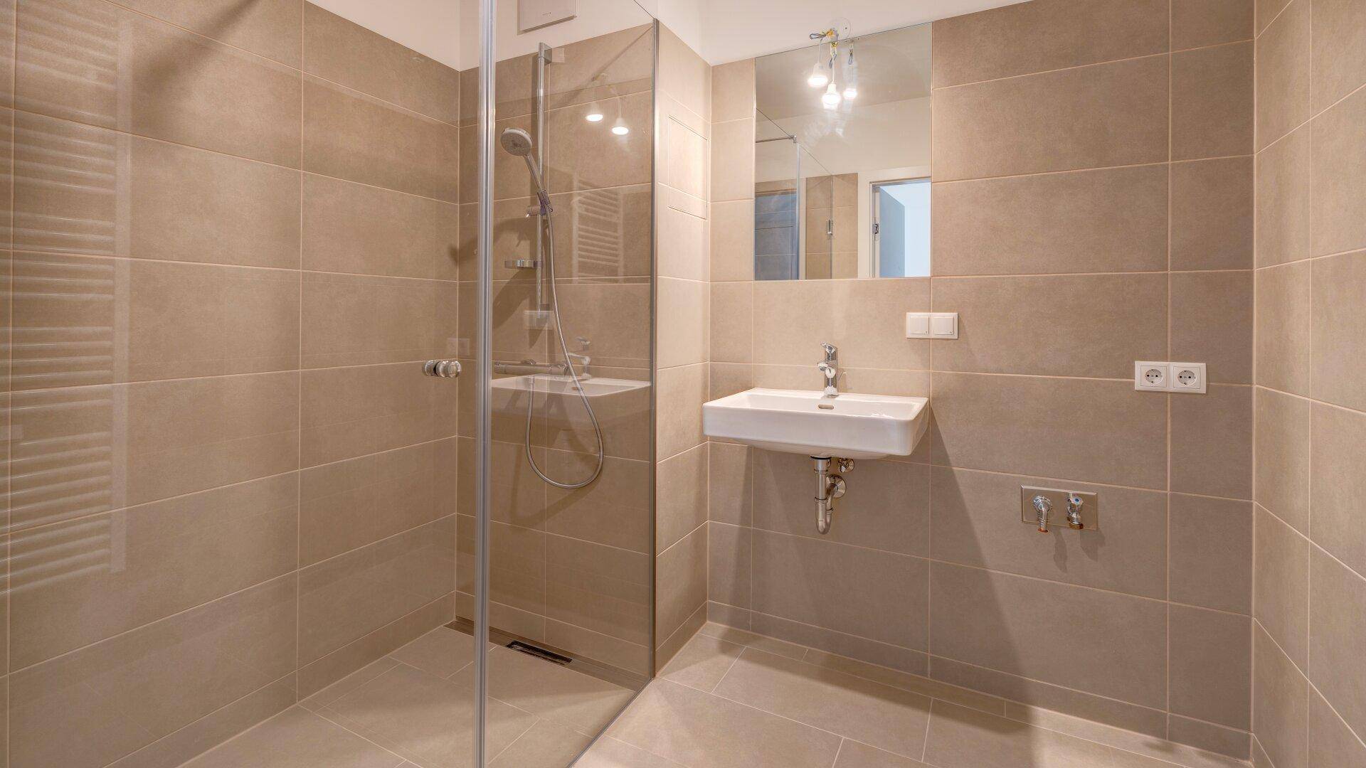 Modernes Badezimmer mit beigefarbenen Fliesen, ebenerdiger Dusche und Waschbecken mit Spiegel.
