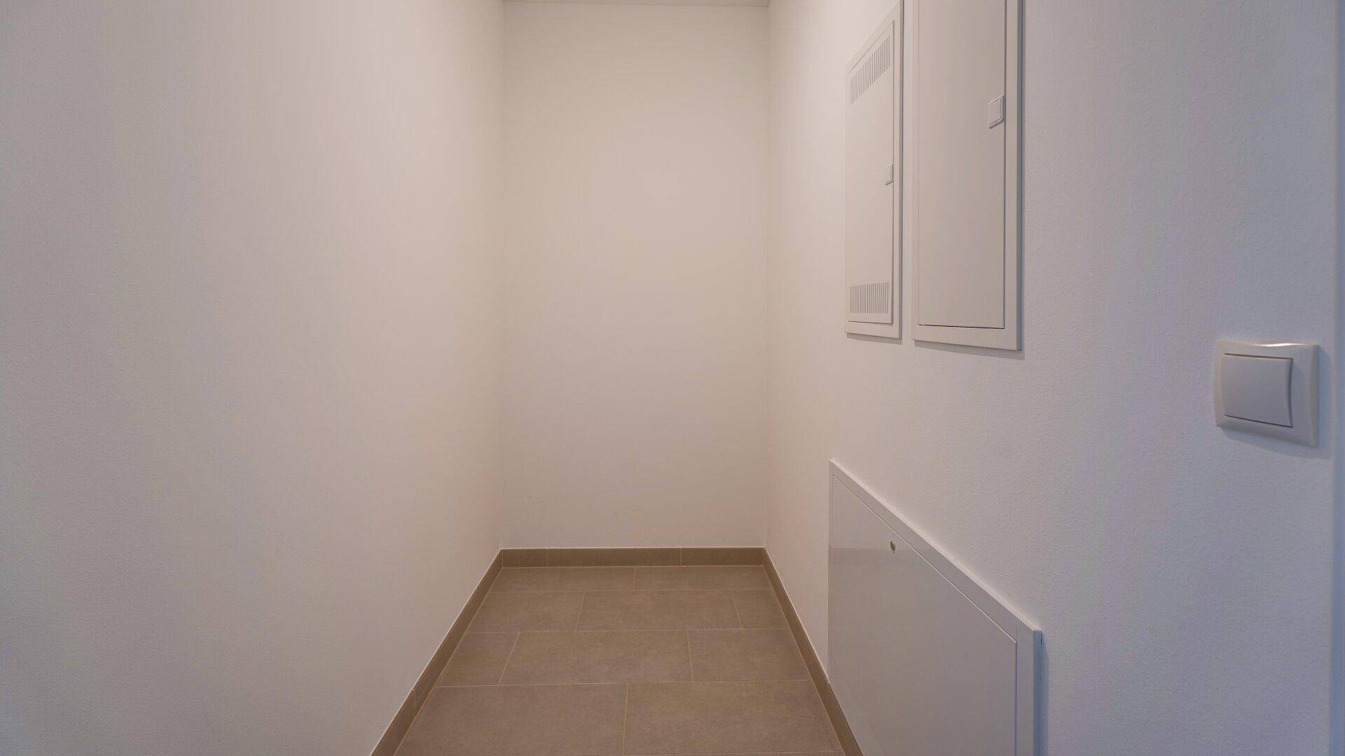 Schmaler Raum mit Fliesenboden und Zugang zu technischen Installationen, ideal als Abstellraum.