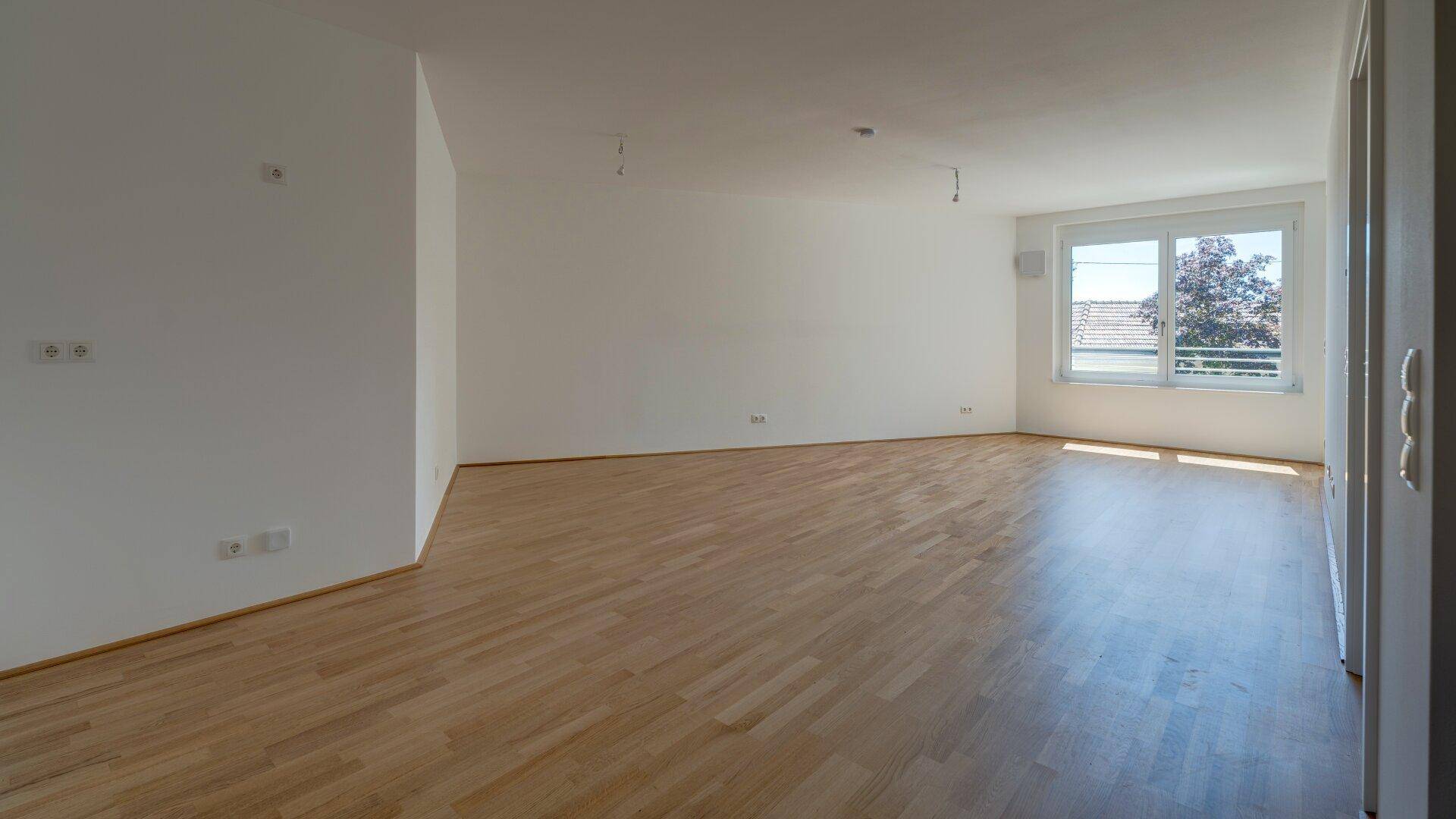 Heller und geräumiger Wohnbereich mit großen Fenstern und hochwertigem Holzparkettboden.