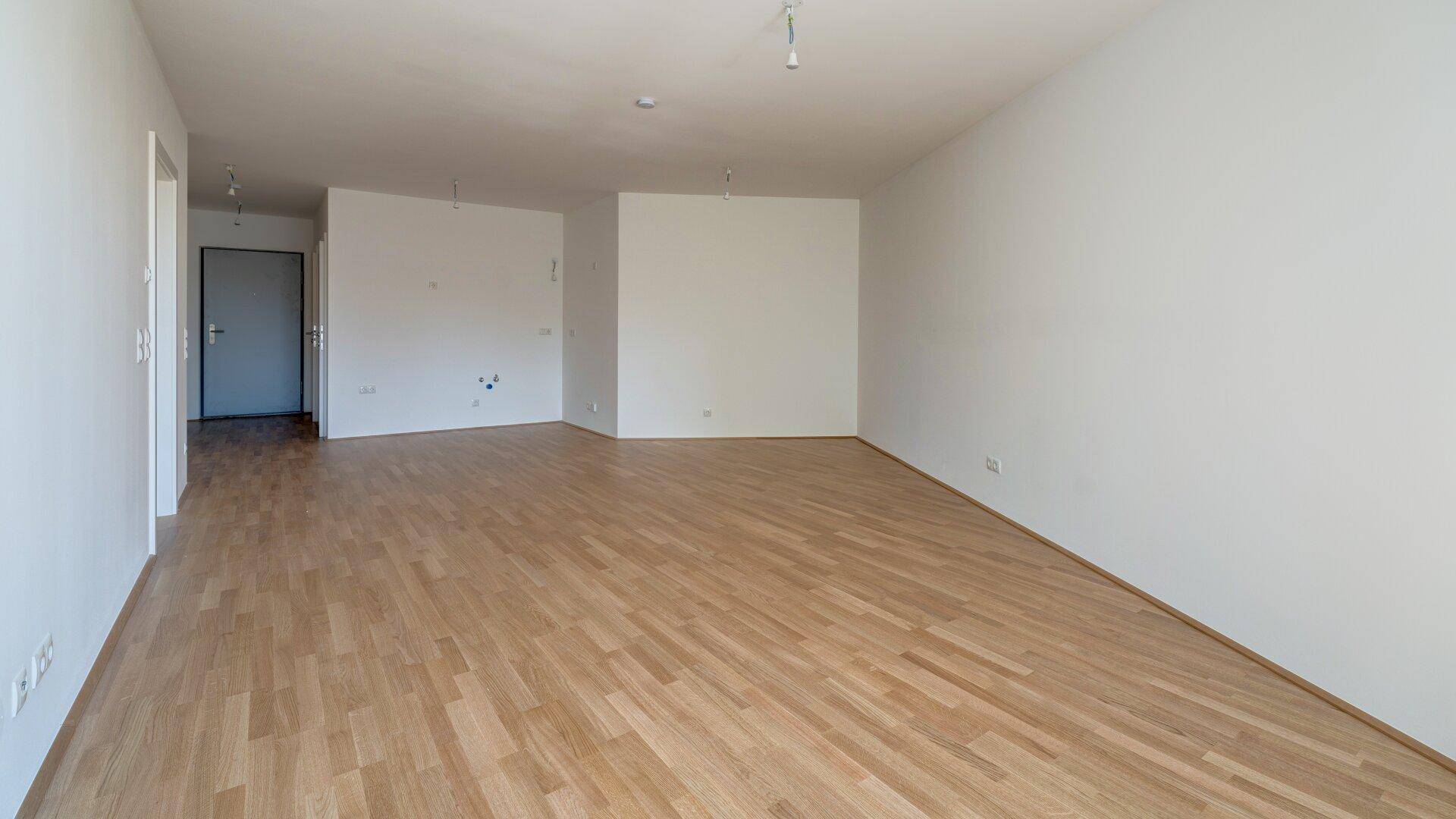 Geräumiges Wohnzimmer mit hellem Holzparkettboden und viel Tageslicht, ideal für offene Wohnkonzepte.