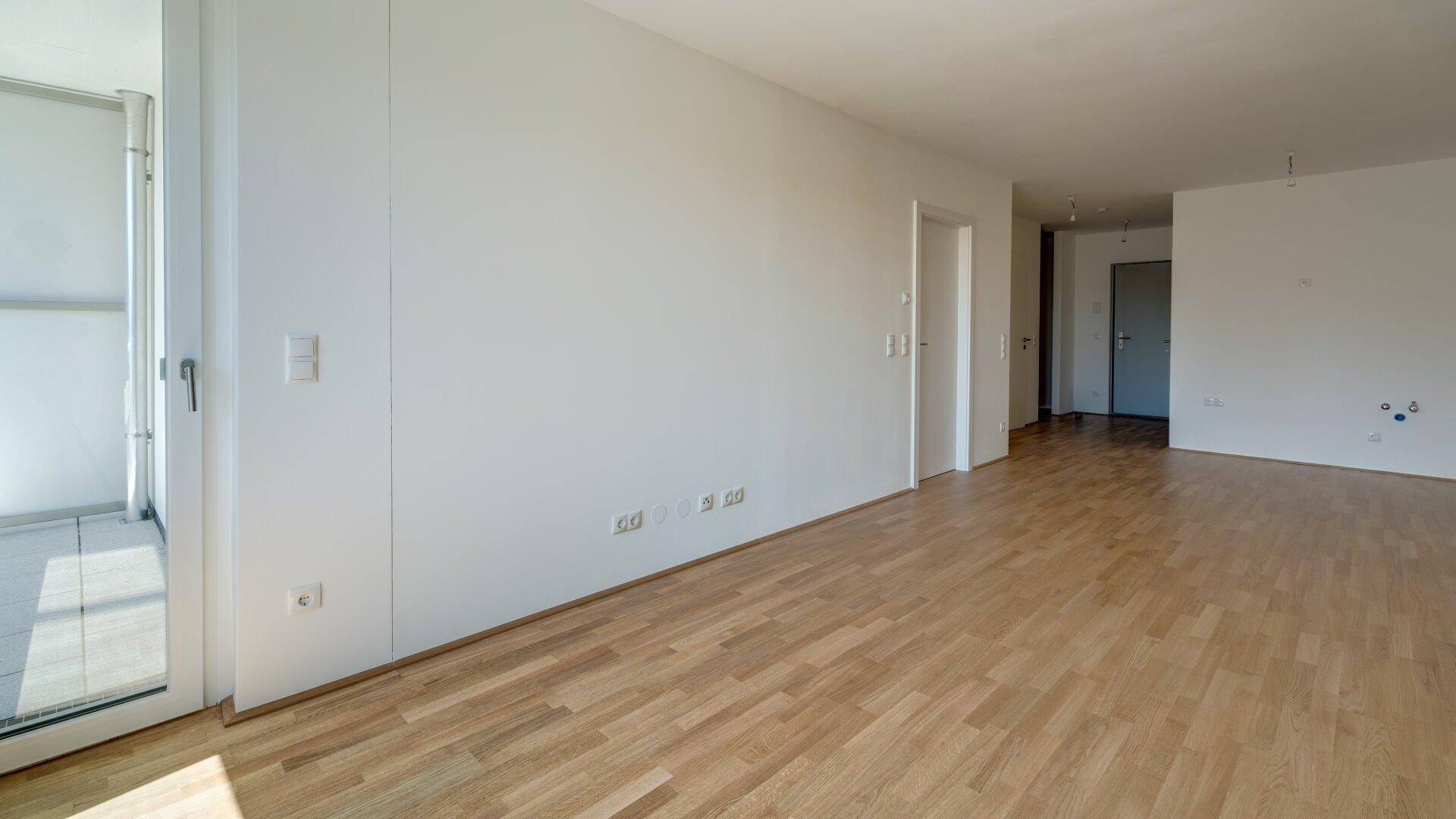 Heller Wohnbereich mit Zugang zum Balkon und Holzparkettboden, bietet viel natürliches Licht.