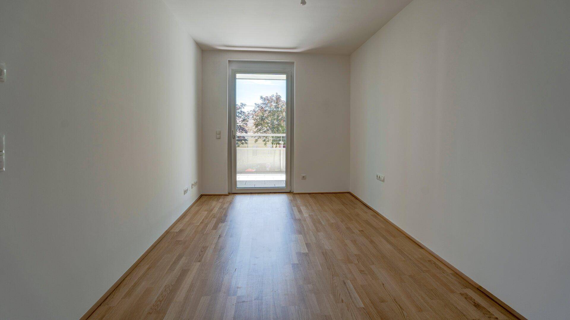 Helles Schlafzimmer mit Holzparkettboden und direktem Zugang zu einem kleinen Balkon.