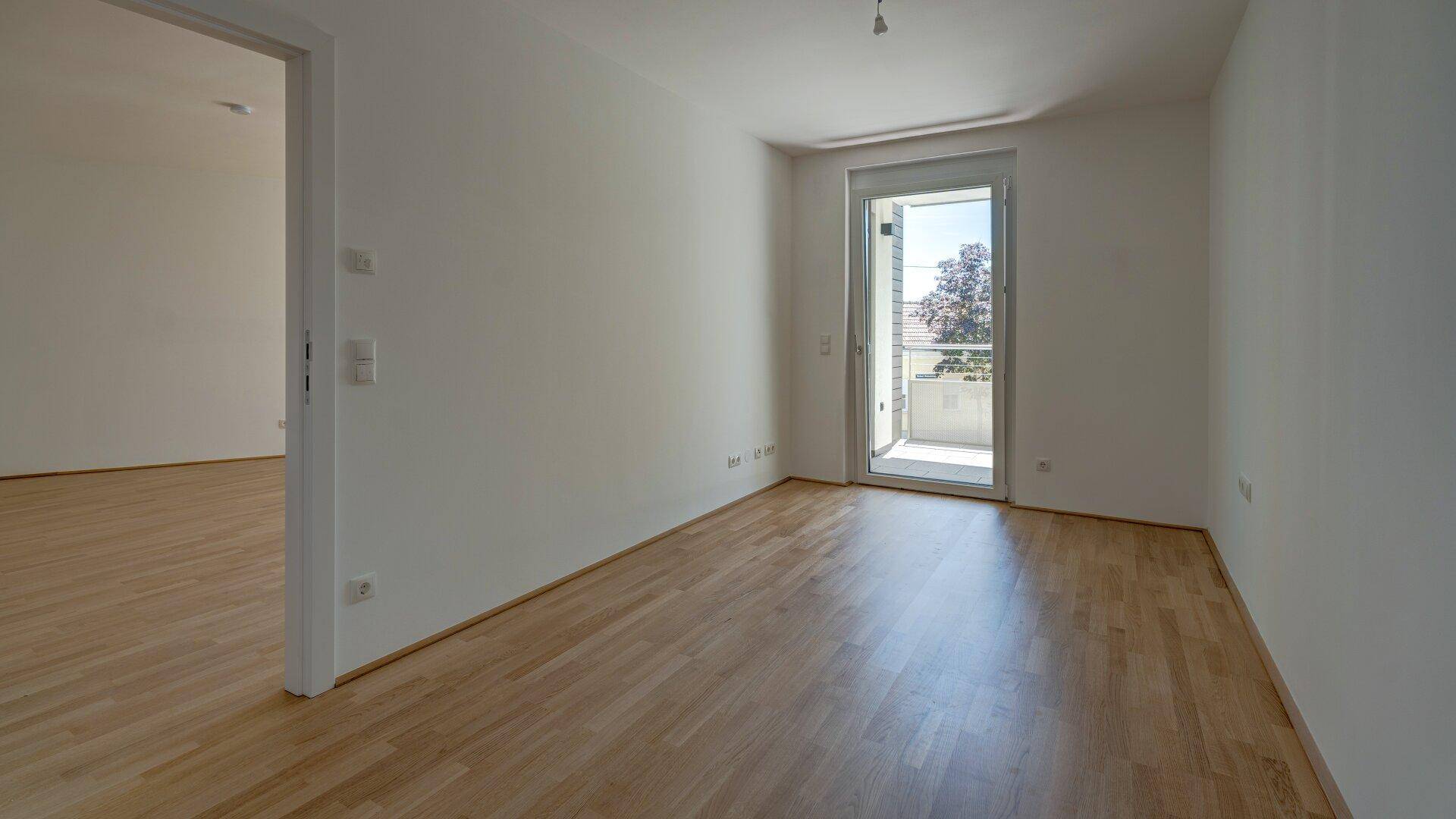 Geräumiges Schlafzimmer mit Holzparkettboden und Balkonzugang, bietet viel Tageslicht und frische Luft.