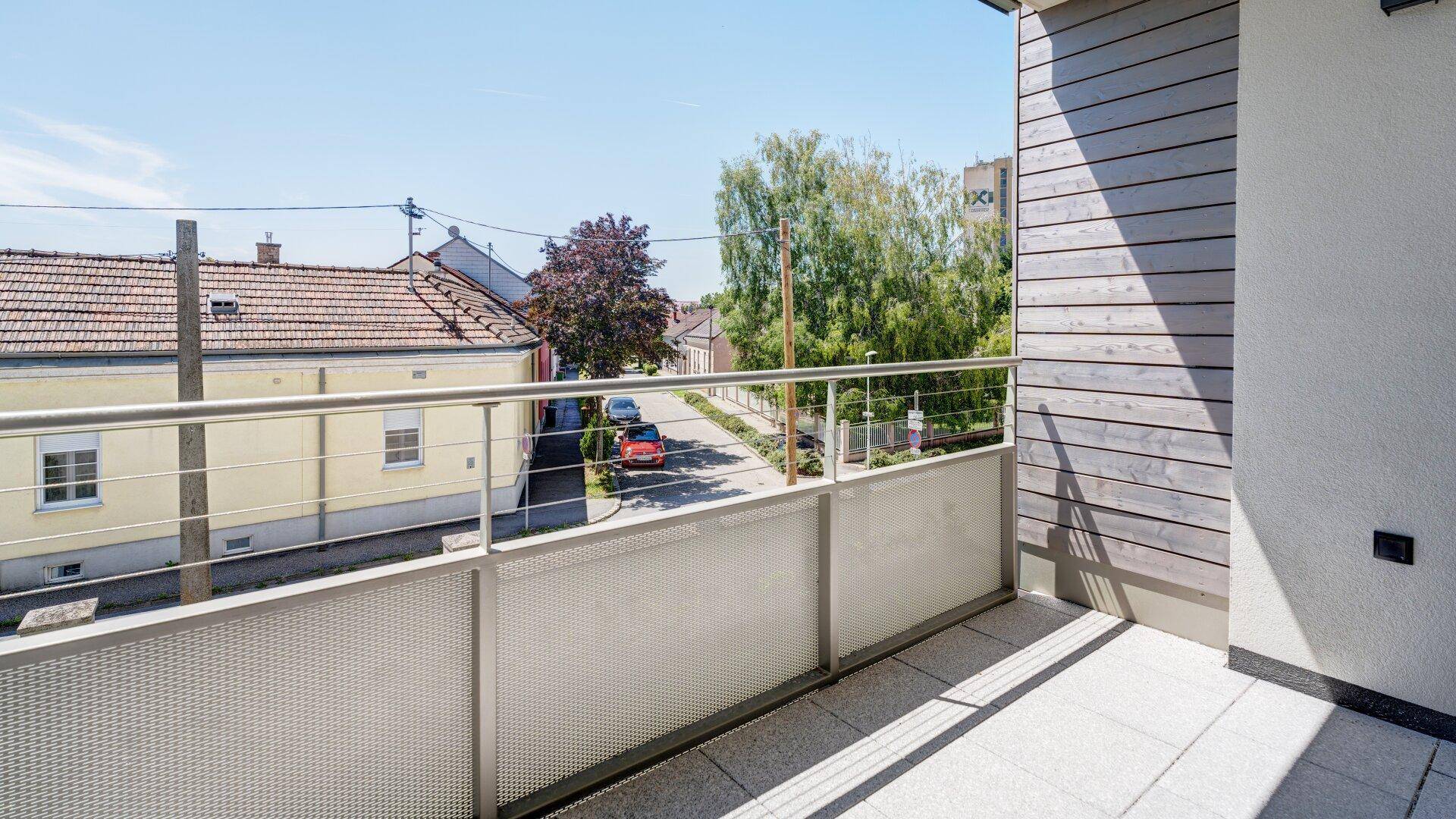 Heller Balkon mit Metallgeländer und Blick auf die umliegende Nachbarschaft und Straße.