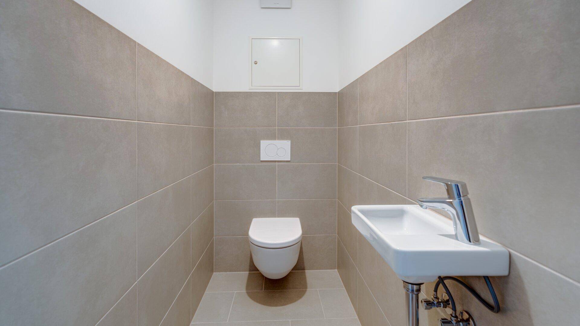 Modernes Gäste-WC mit wandhängender Toilette, kleinem Waschbecken und beigefarbenen Fliesen.