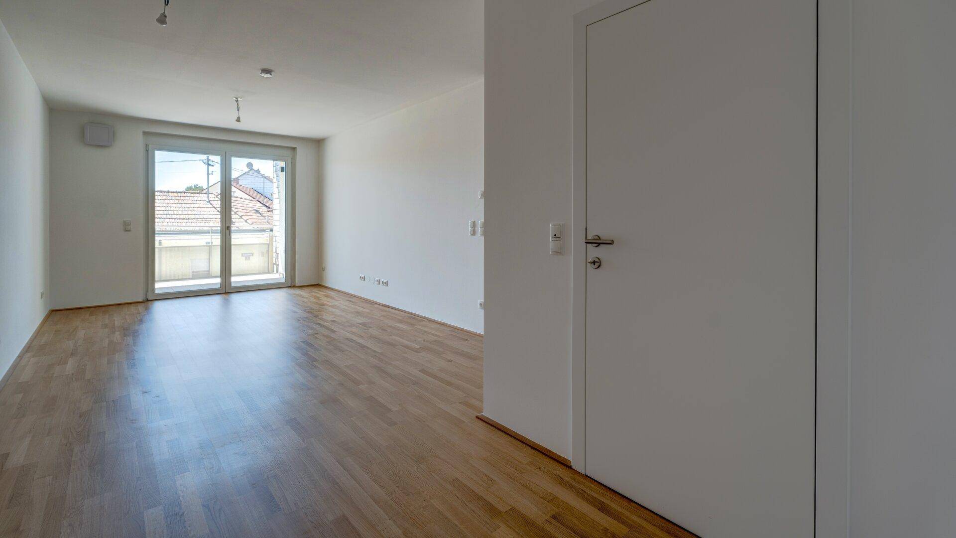 Heller Wohnbereich mit Holzparkettboden und Zugang zu einem Balkon, der viel Licht spendet.