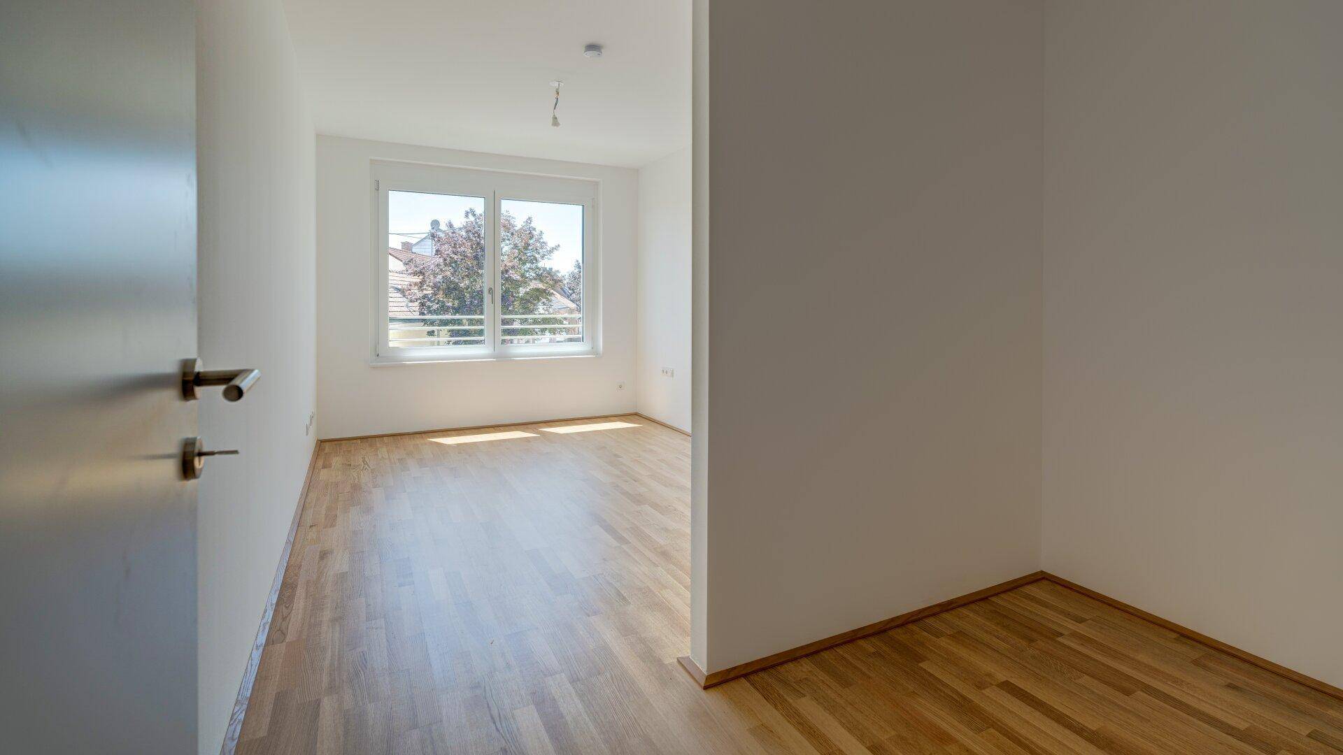 Heller Flur mit Holzparkettboden, der zu einem weiteren Zimmer mit Fenster führt.