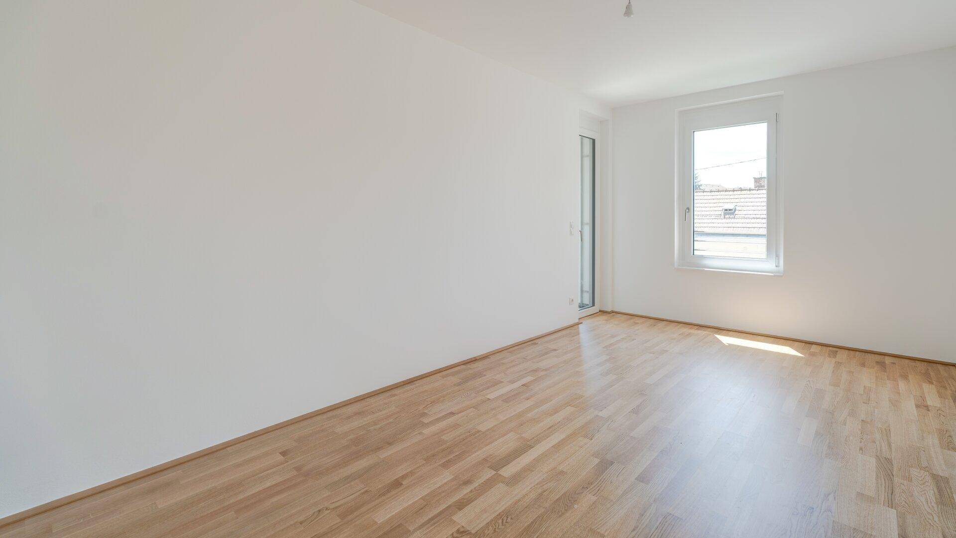 Heller Raum mit Holzparkettboden und einem Fenster, das viel Tageslicht hereinlässt.