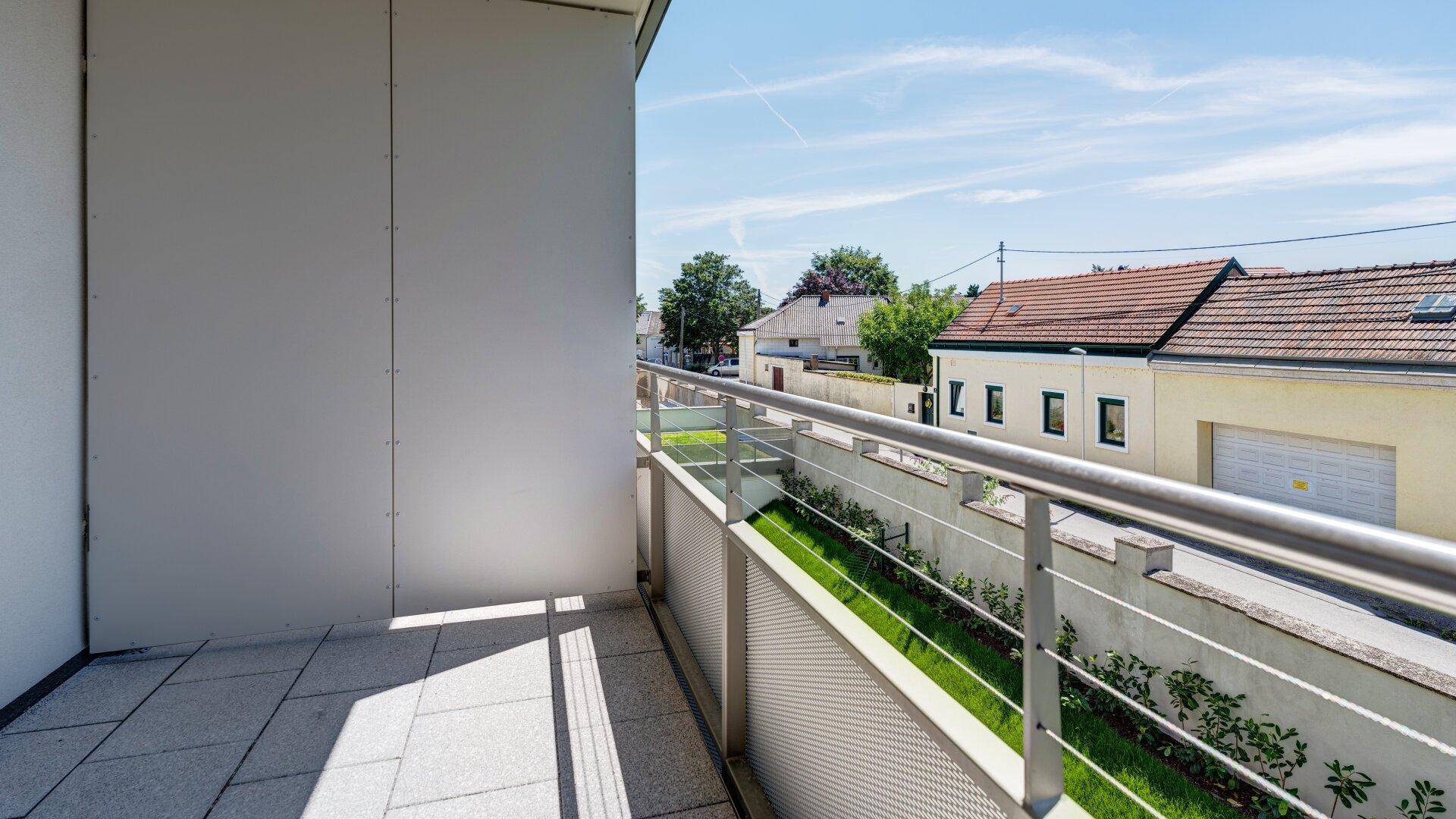 Langer Balkon mit Metallgeländer und Blick auf die umliegende Nachbarschaft und Grünflächen.