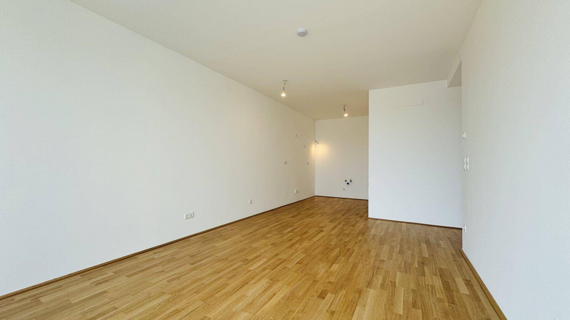 Großer, offener Raum mit hellem Holzboden und weißen Wänden, ideal für flexible Wohnkonzepte.