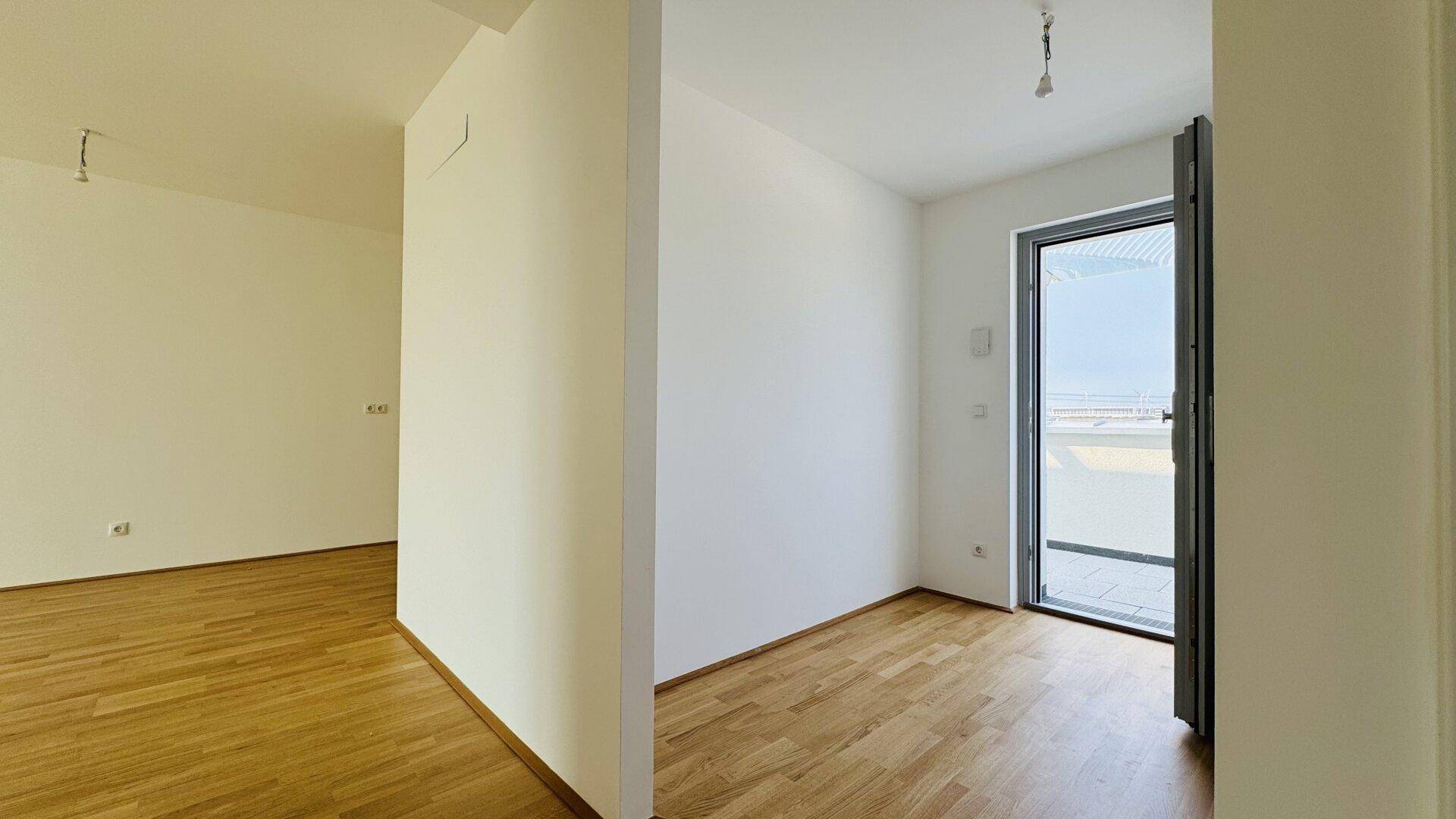 Heller Raum mit Holzboden und Glastür, die zu einem Außenbereich führt und viel Licht spendet.