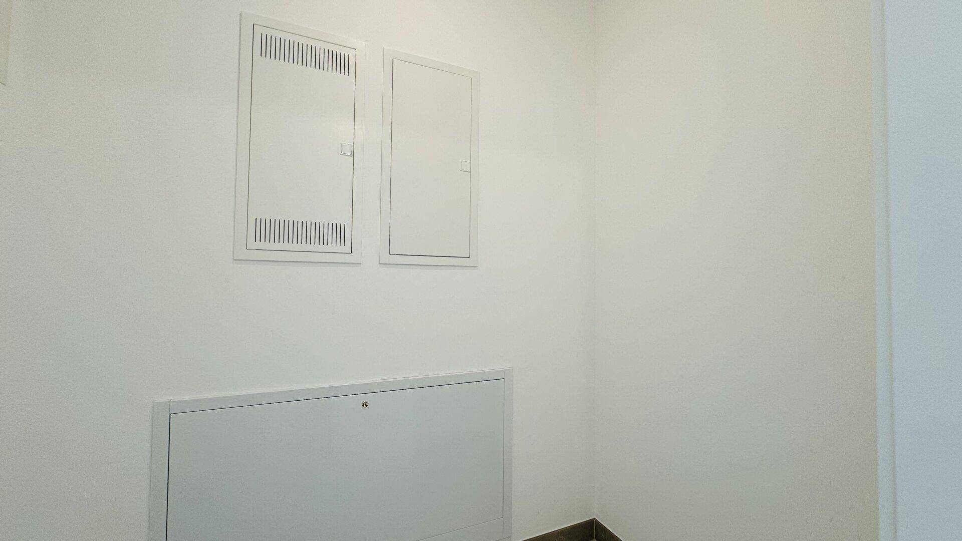 Weiße Wand mit drei integrierten Wartungsklappen, die Zugang zu Versorgungseinrichtungen bieten.