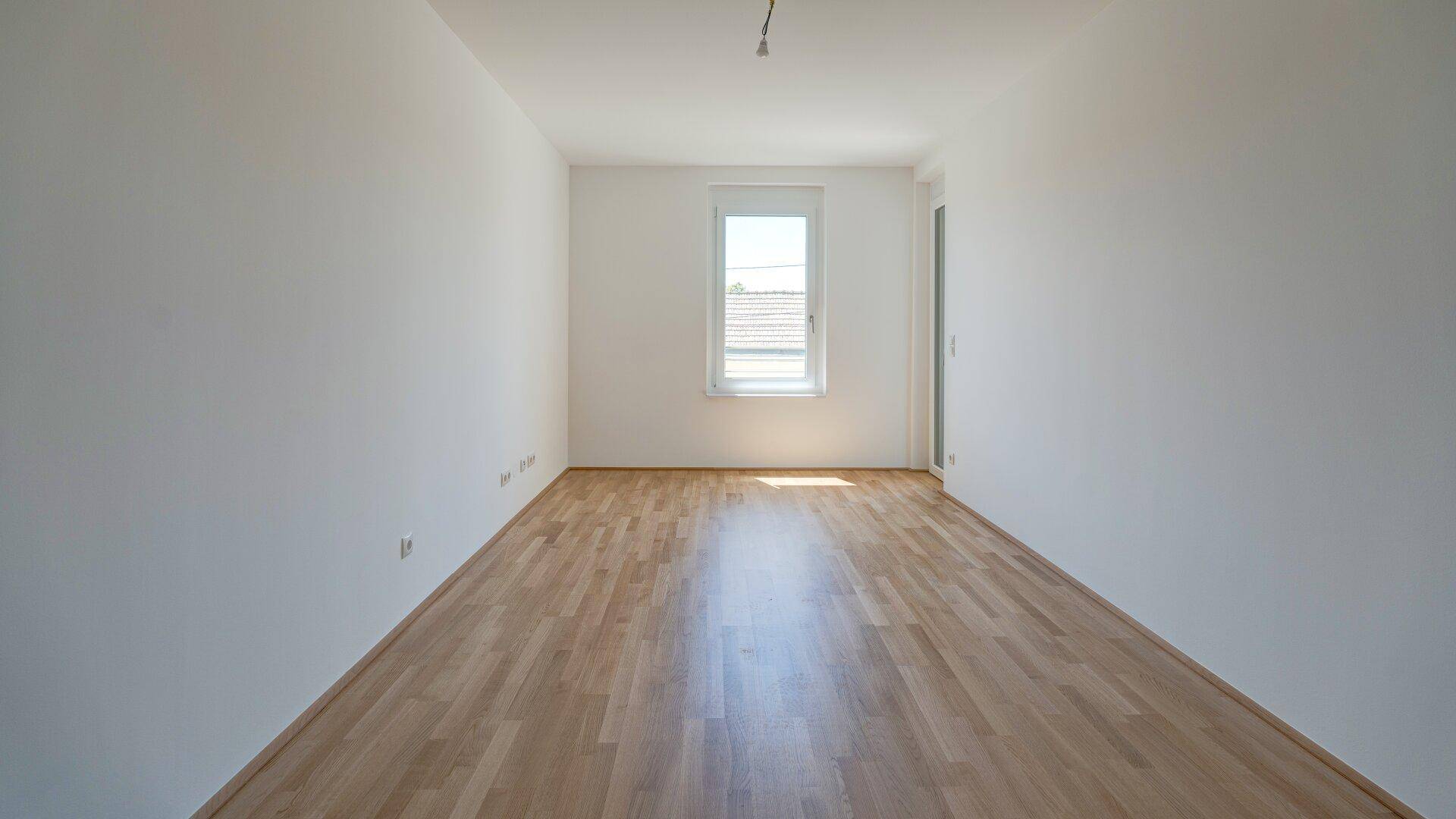 Ruhiges, helles Zimmer mit Holzboden und einem Fenster, ideal als Schlaf- oder Arbeitszimmer.
