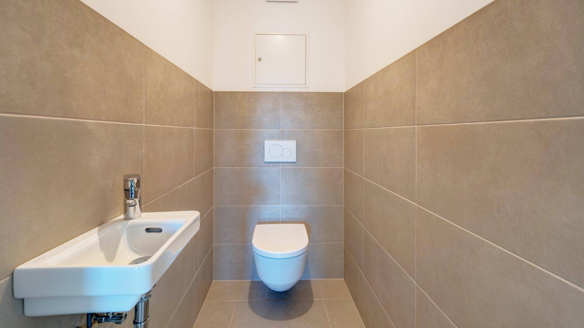Modernes Gäste-WC mit beigefarbenen Fliesen, wandhängendem WC und kleinem Waschbecken.