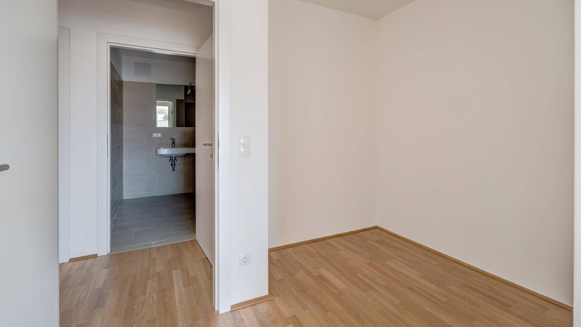 Leeres Zimmer mit Holzboden und direktem Zugang zu einem modernen Badezimmer.
