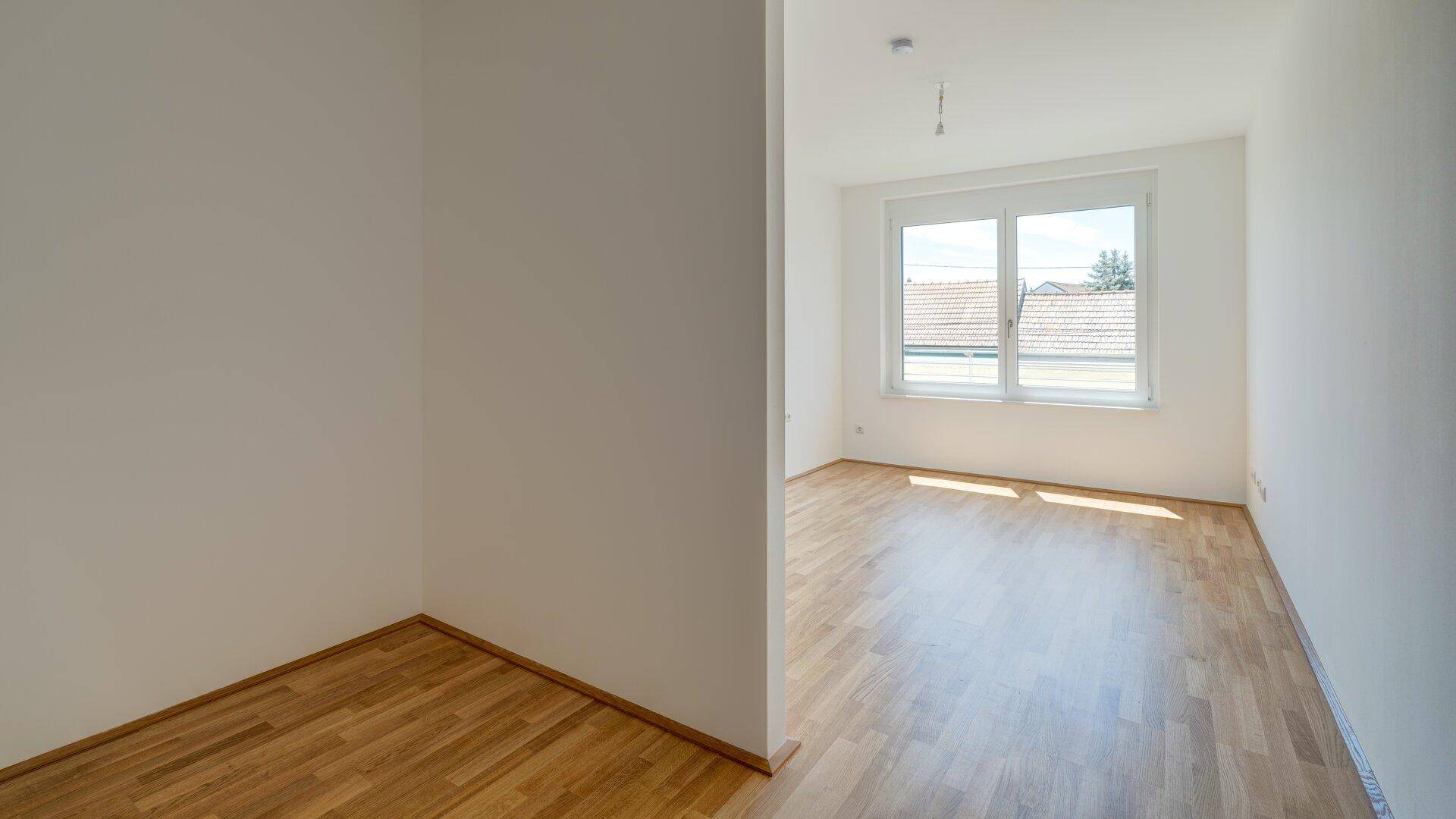 Helles Zimmer mit Holzboden und Fenster, bietet viel Tageslicht und eine angenehme Atmosphäre.