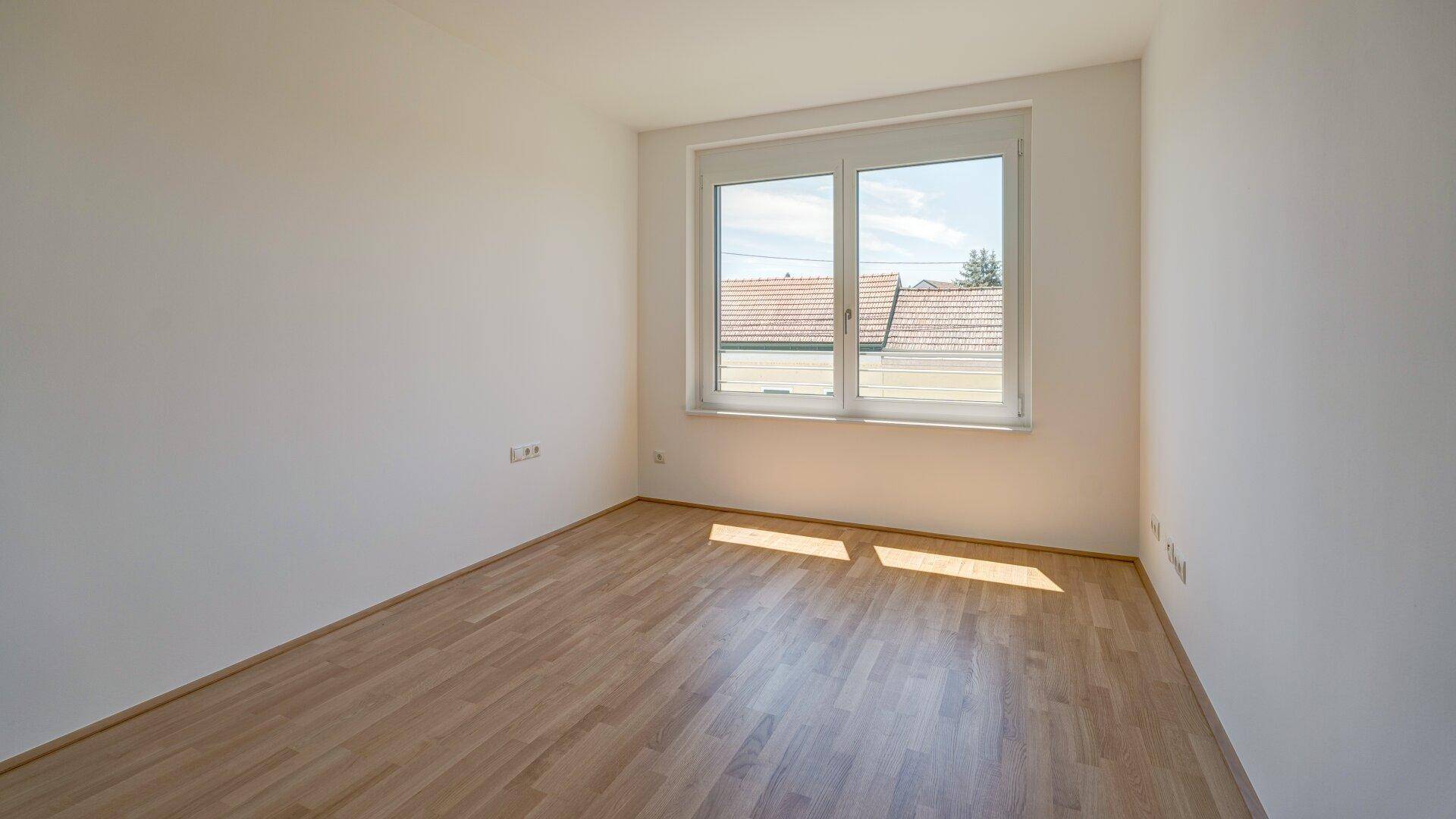 Helles Zimmer mit Holzboden und großem Fenster, ideal als Schlaf- oder Kinderzimmer.