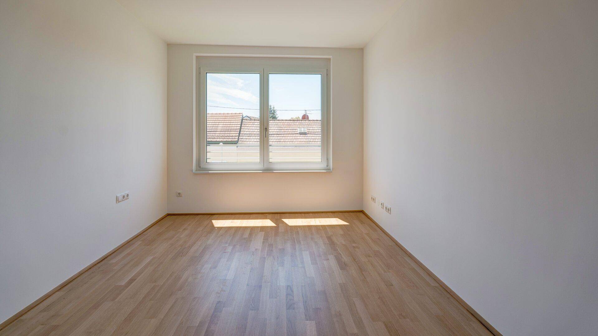 Lichtdurchflutetes Zimmer mit Holzboden und Fenster, bietet eine ruhige und helle Umgebung.