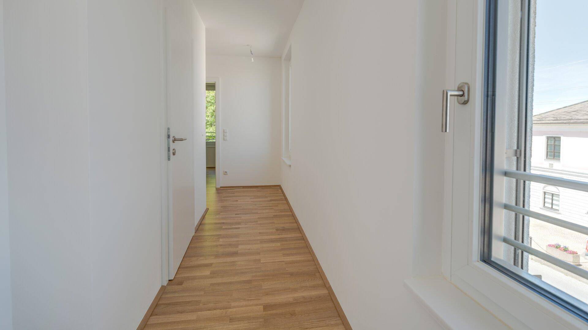 Heller Flur mit modernem Holzparkettboden und einem Fenster, das Tageslicht hereinlässt.