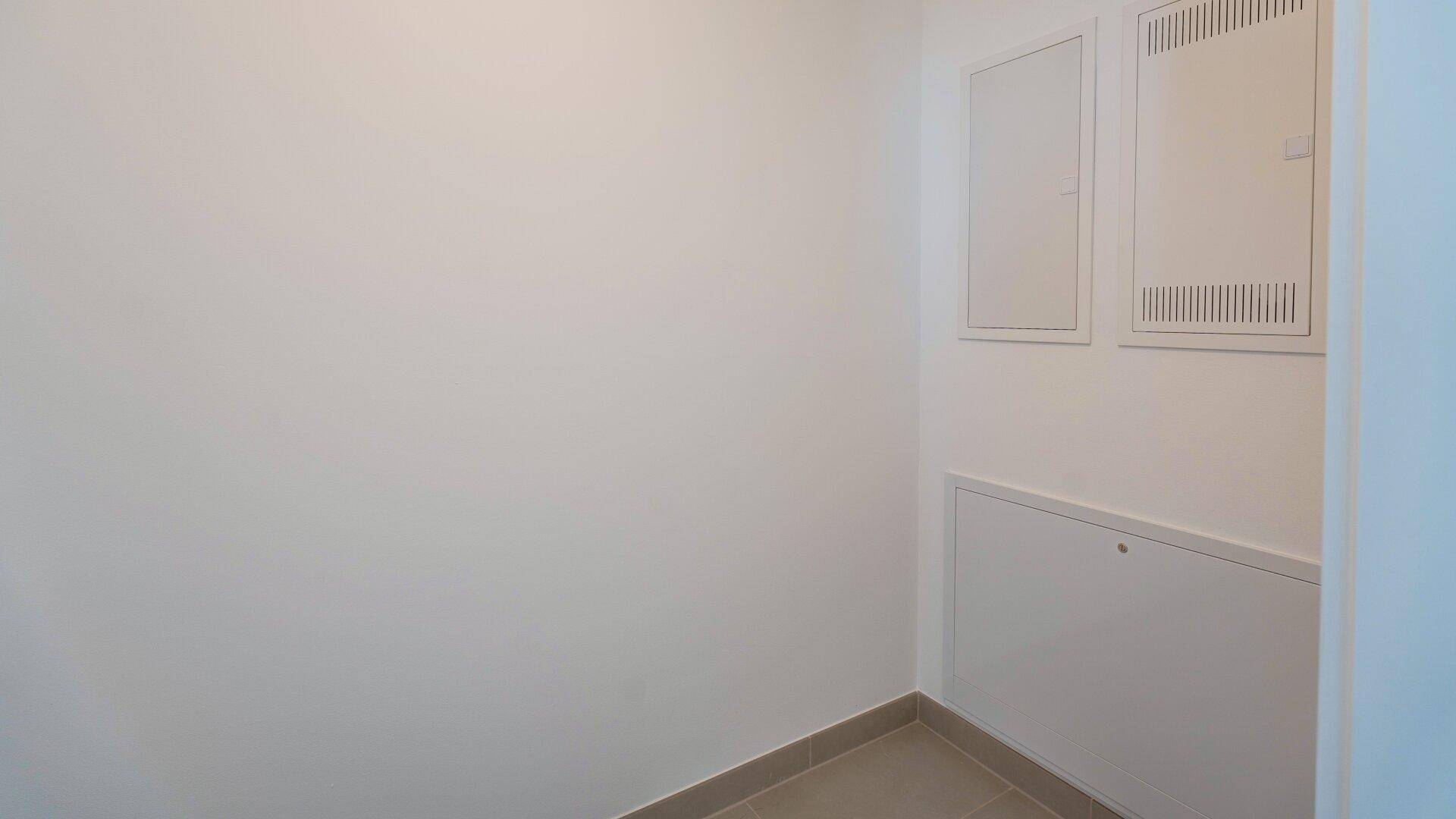 Kleiner Abstellraum mit hellen Wänden und Fliesenboden, ausgestattet mit Versorgungspaneelen.