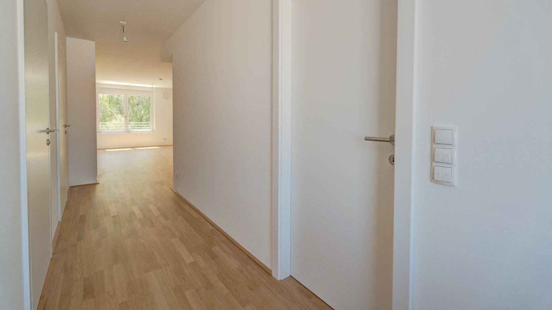 Geräumiger Flur mit hellem Holzparkett und weißen Türen, der zu weiteren Zimmern führt.